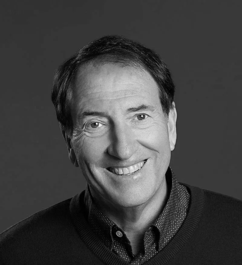 Black and white portrait of David Shelmerdine AO, a smiling middle-aged man with dark hair, wearing a dark sweater and collared shirt.