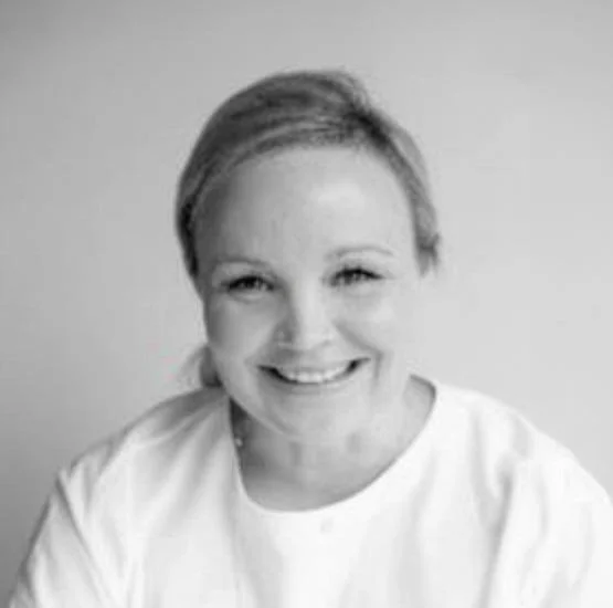 Black and white photo of Vanessa Gibbons, a smiling woman with short hair, wearing a white shirt, facing the camera.
