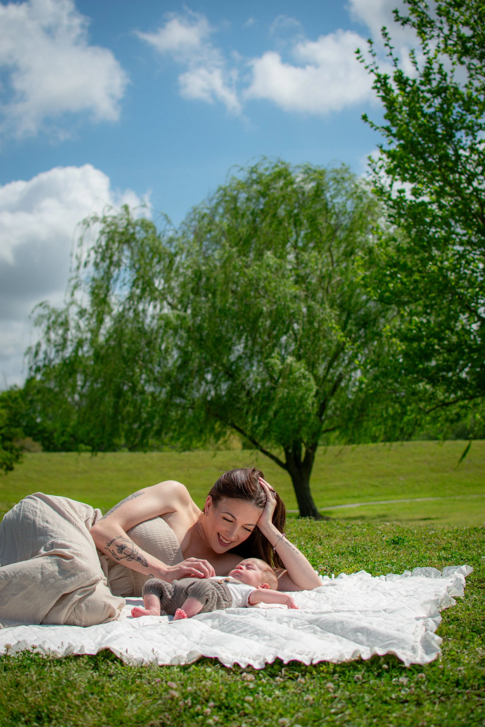 Mother lying beside her baby on a white blanket during an outdoor family photography session in Jacksonville, North Carolina.