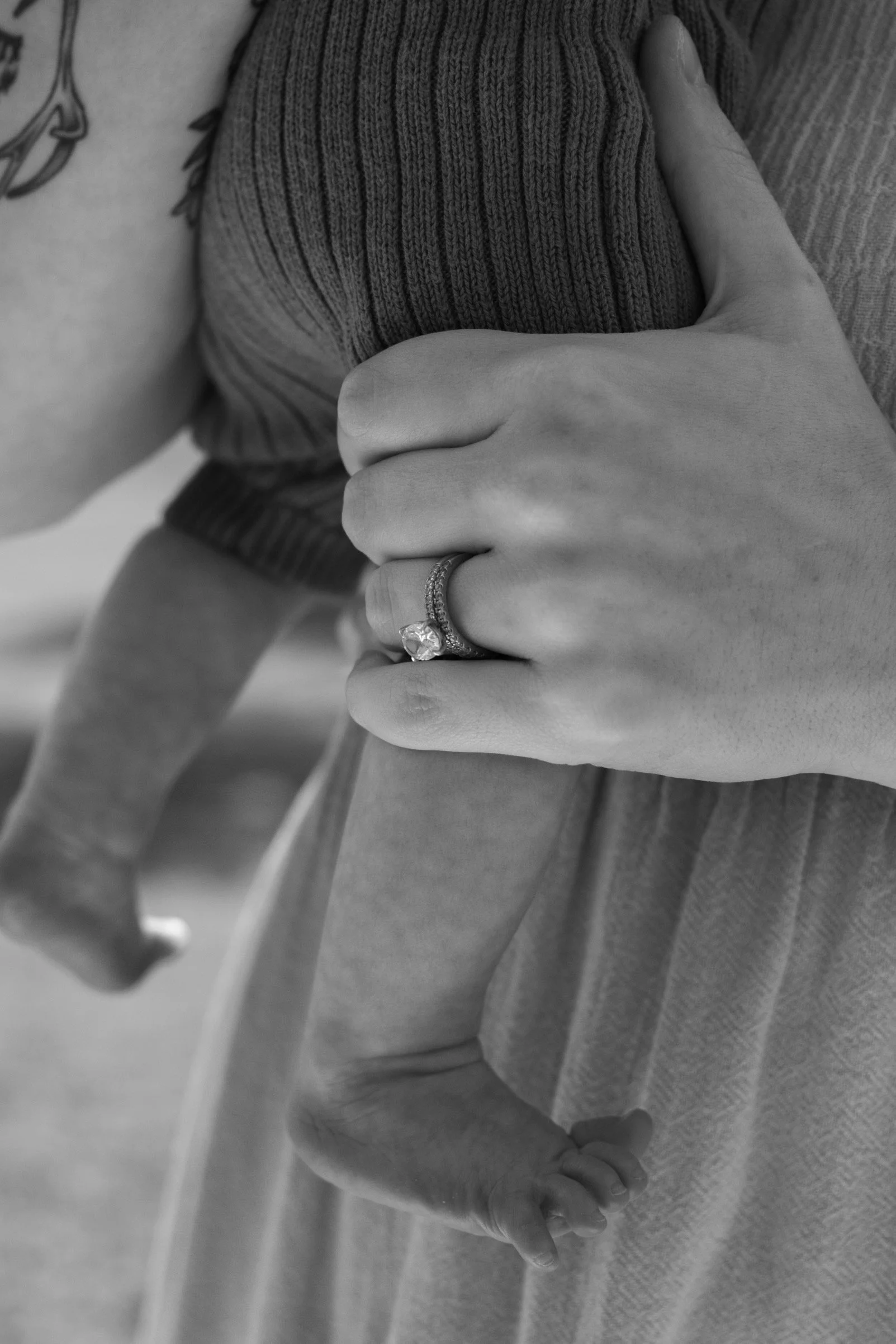 Close-up detail of a mother holding her baby, highlighting her wedding ring during a newborn photography session.