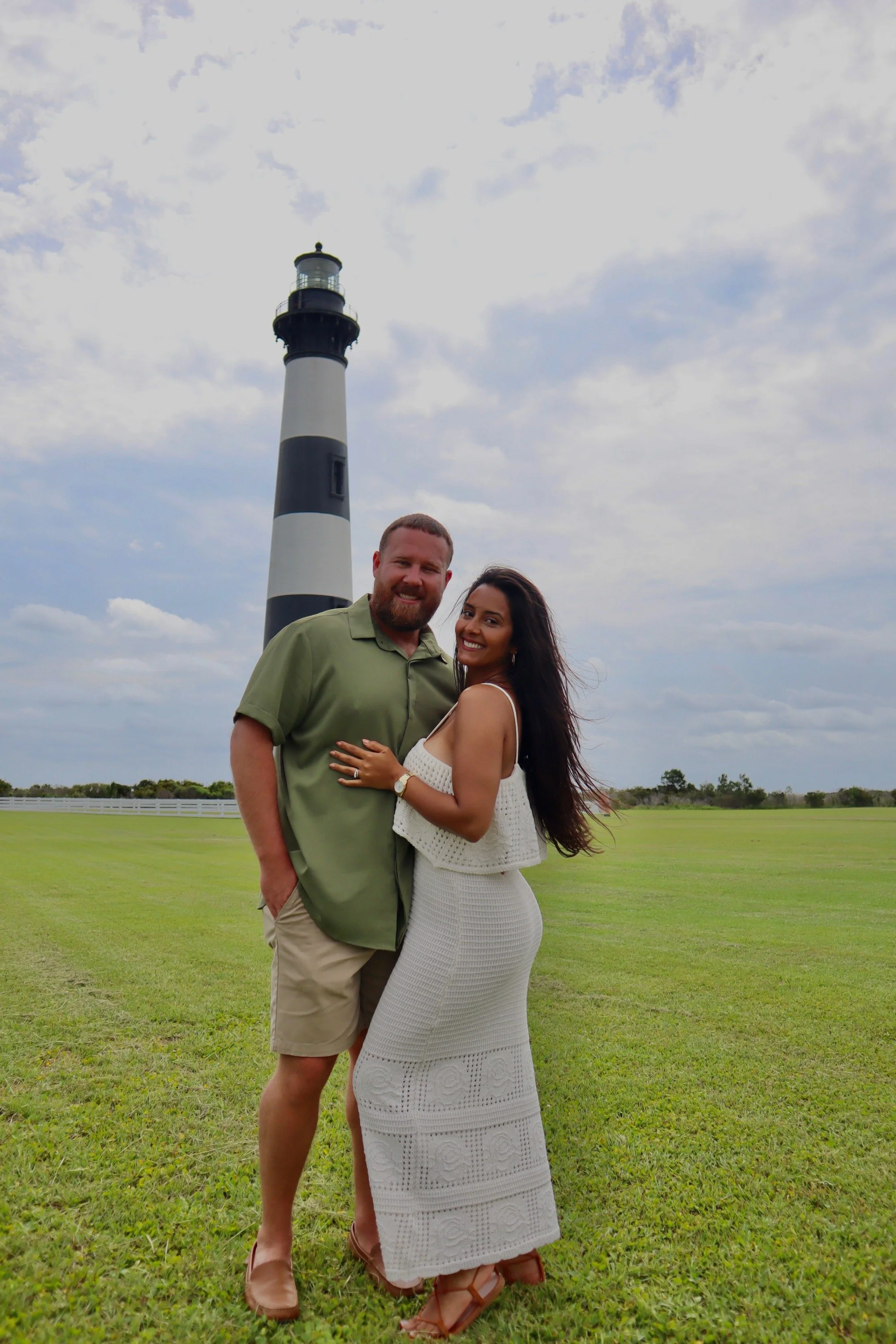 Engaged couple posing in front of Bodie Island Lighthouse during a coastal engagement photography session.