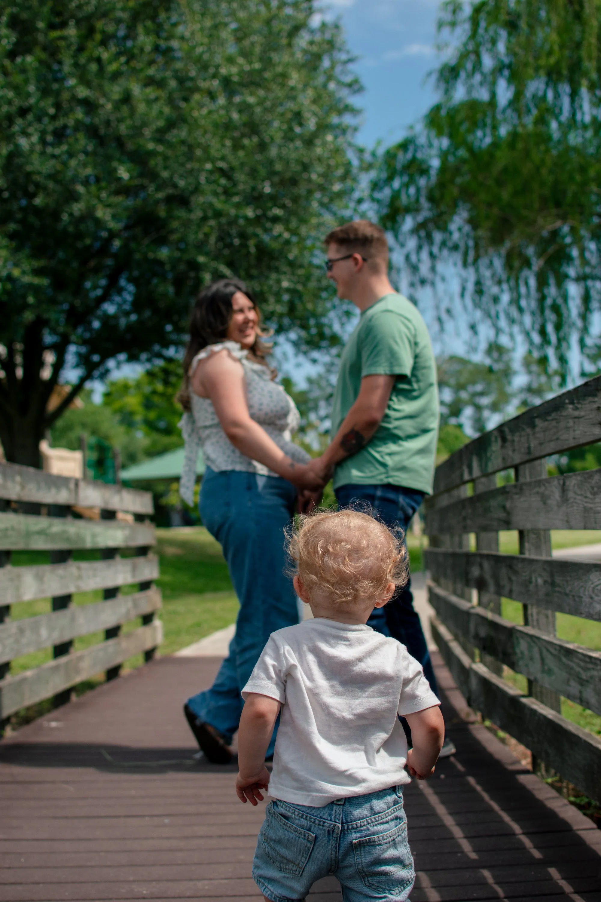 Toddler walking toward parents on a wooden bridge during a family photo session in Jacksonville NC.