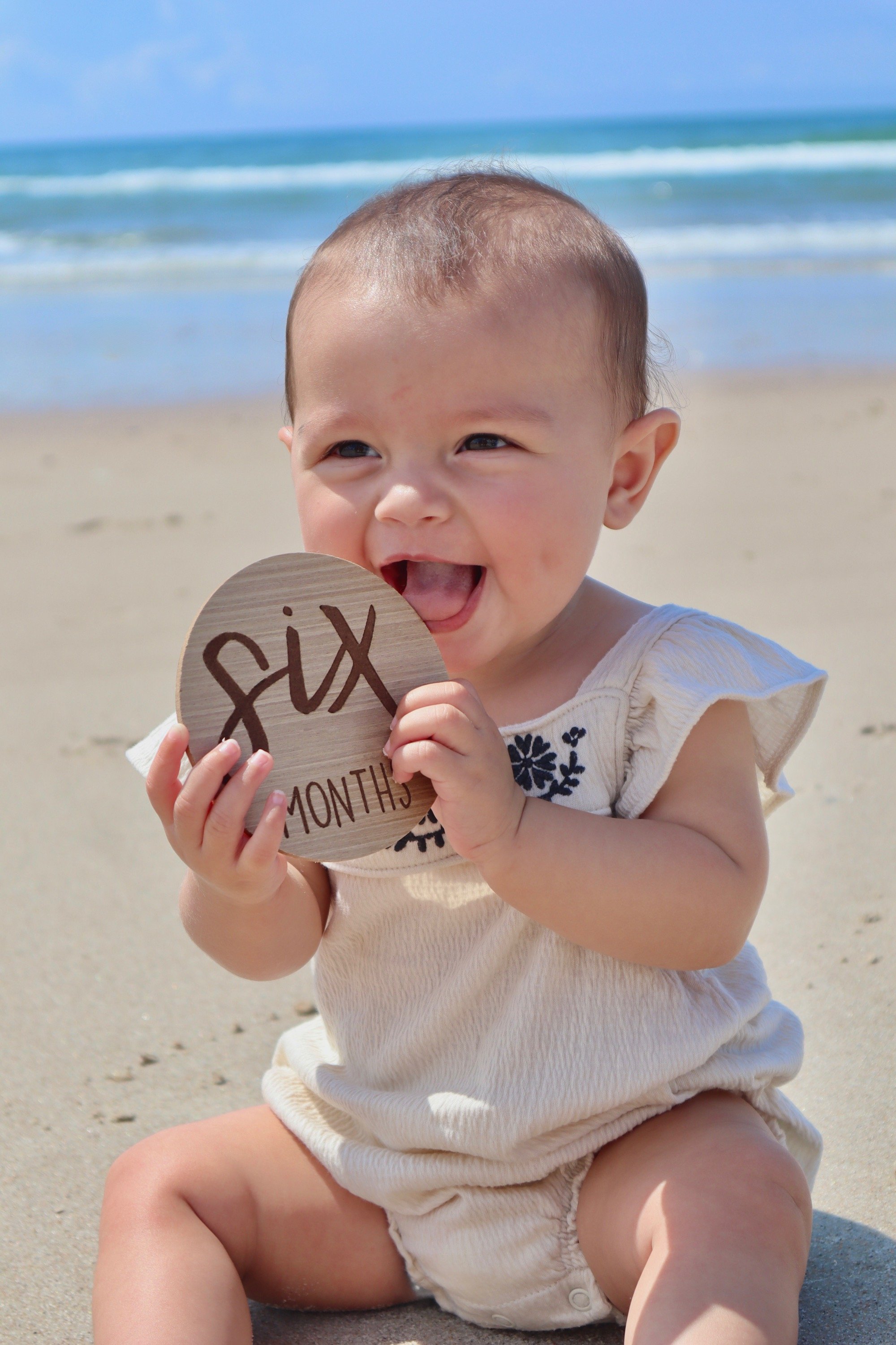Six-month-old baby holding a milestone sign during a beach photography session