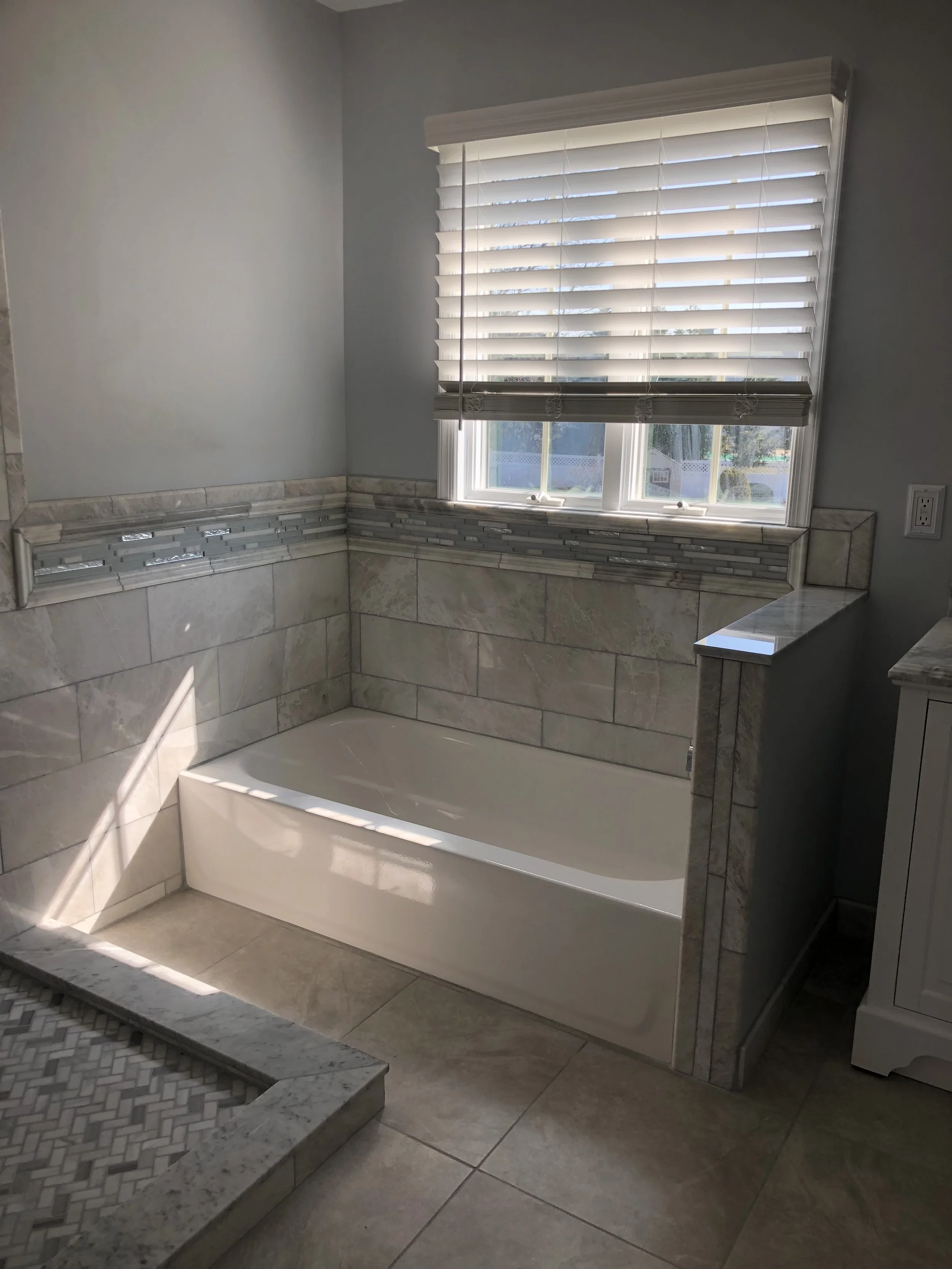 Interior of a bathroom with a bathtub, stone tiled walls, and a window with white blinds.