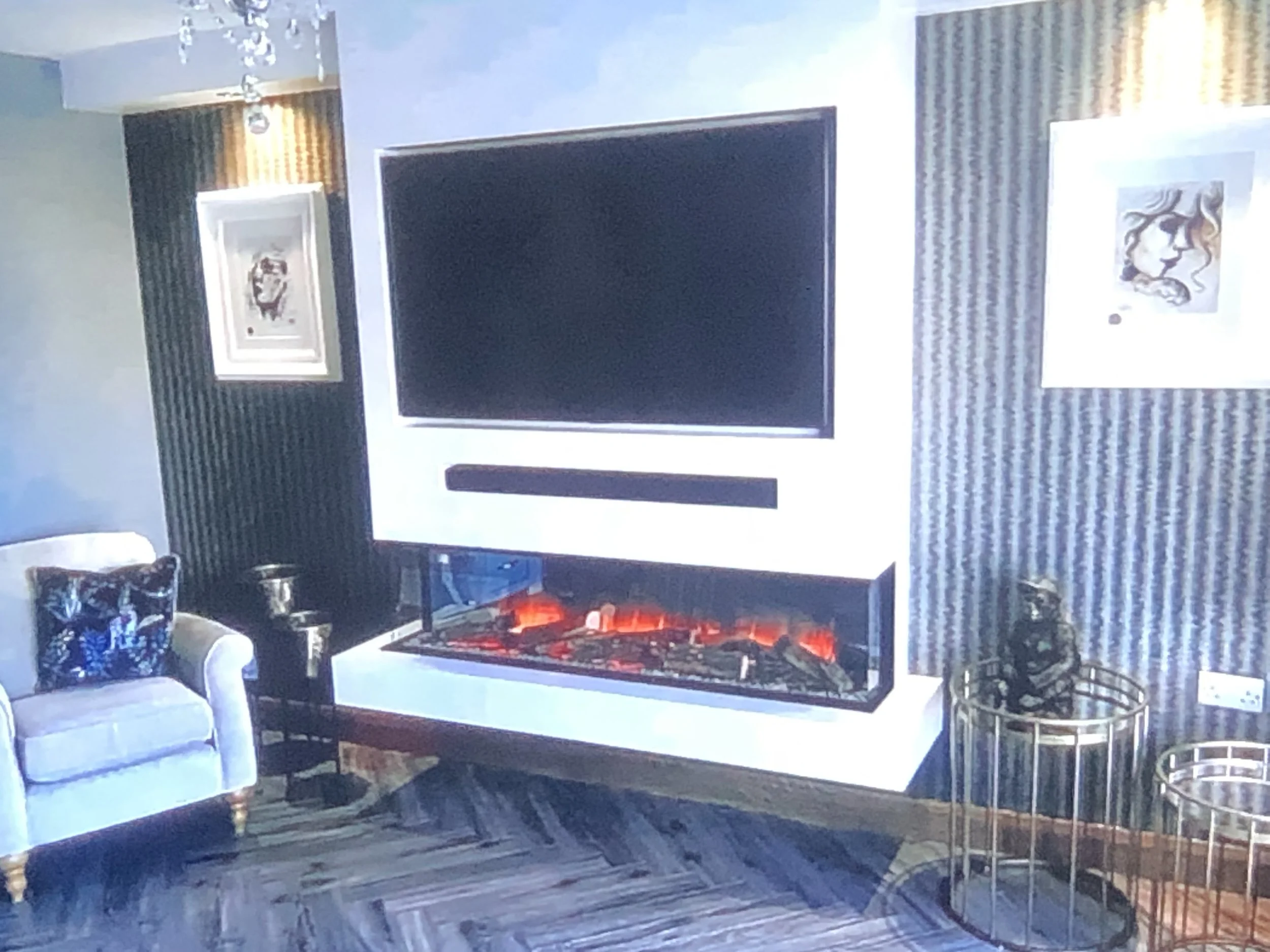 Living room with a large flat-screen TV, a white sofa, a fireplace with decorative fires, a painting of a lion, and a glass coffee table with metal legs.