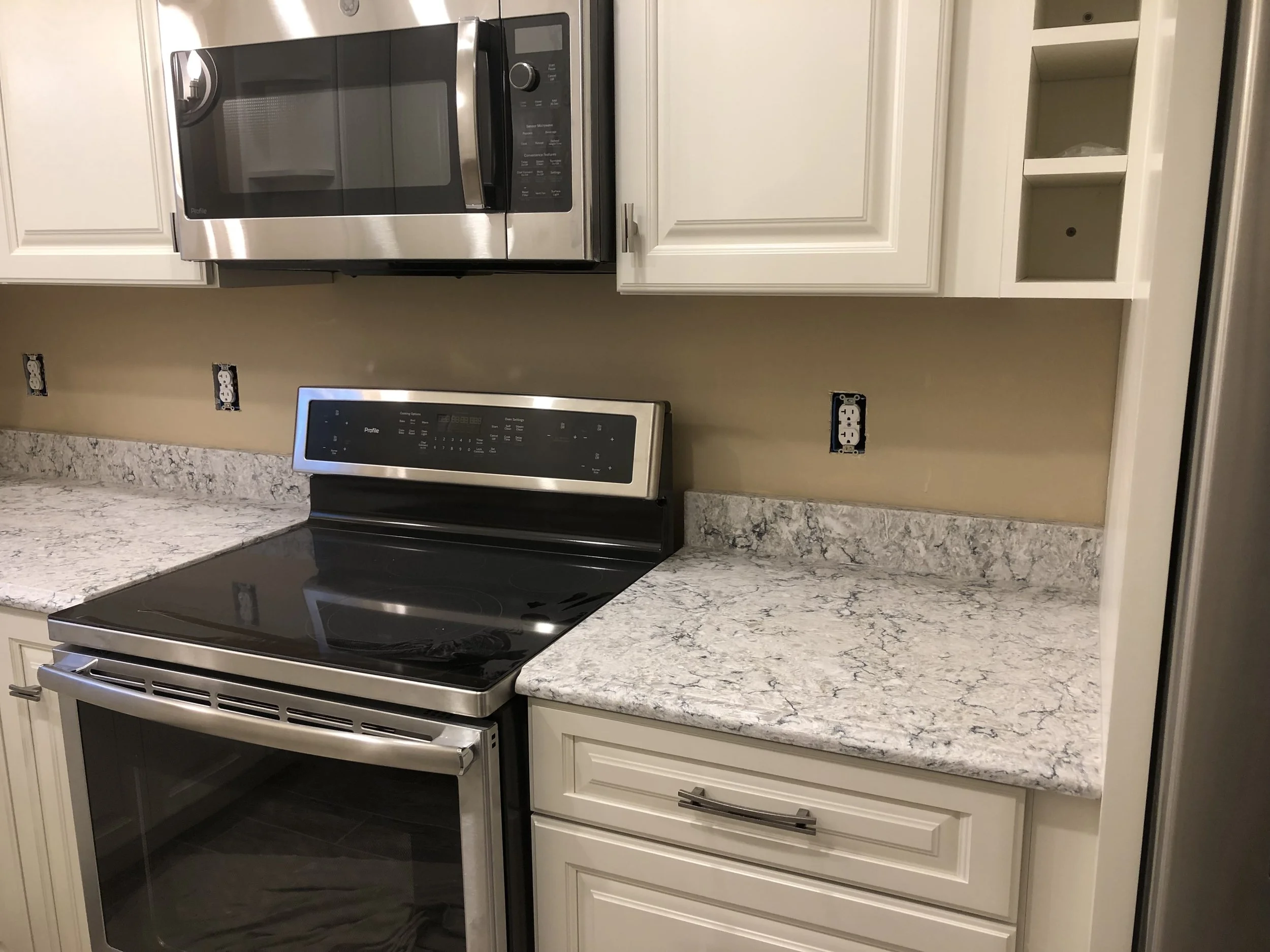 Kitchen with white cabinets, granite countertops, stainless steel microwave and stove, and electrical outlets on the wall.