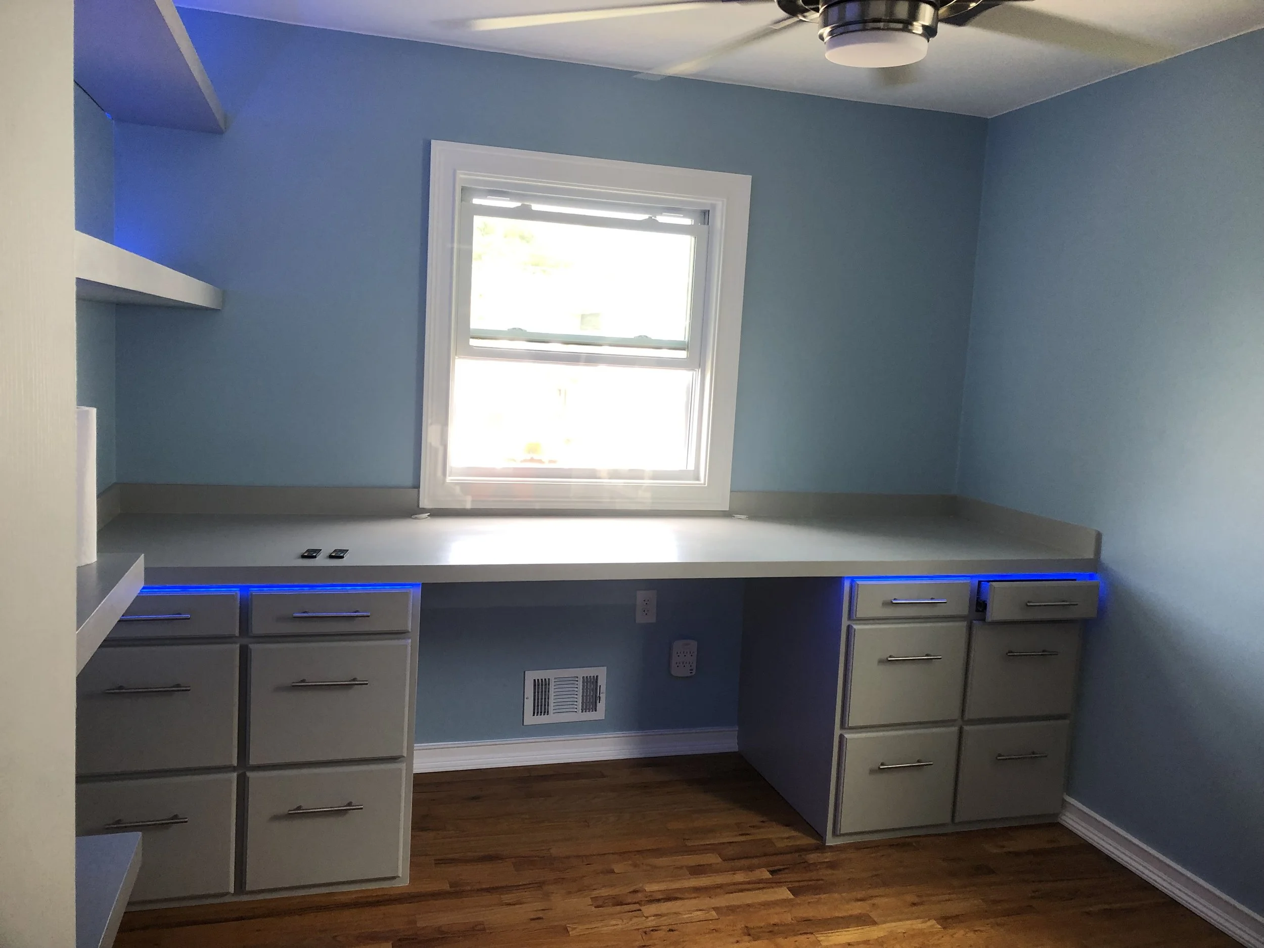 Kitchen with blue painted walls, a window with white trim, gray cabinets with drawers, and hardwood flooring.