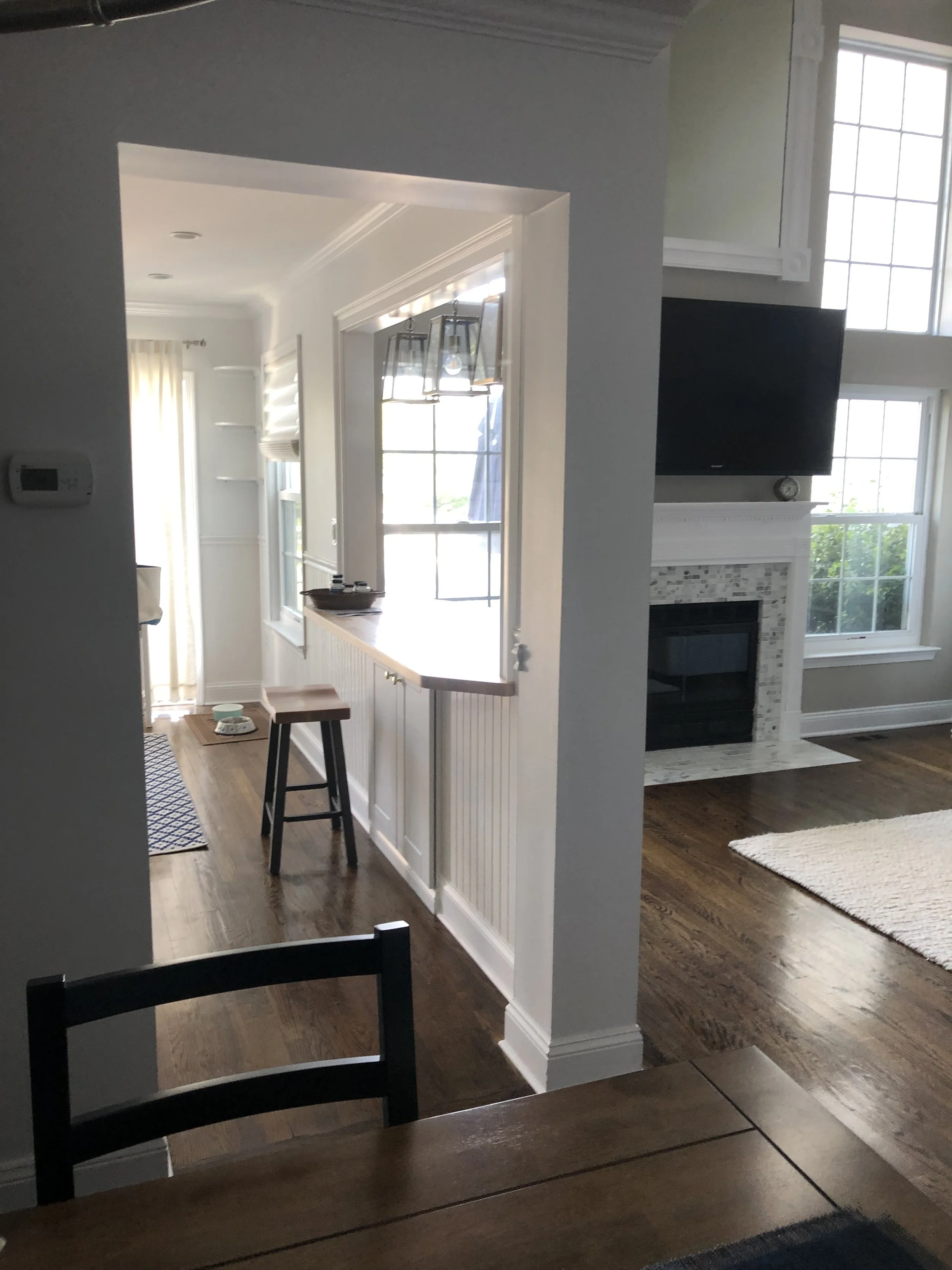 Interior view of a home with a living room and a kitchen, featuring windows, a fireplace, and hardwood floors.