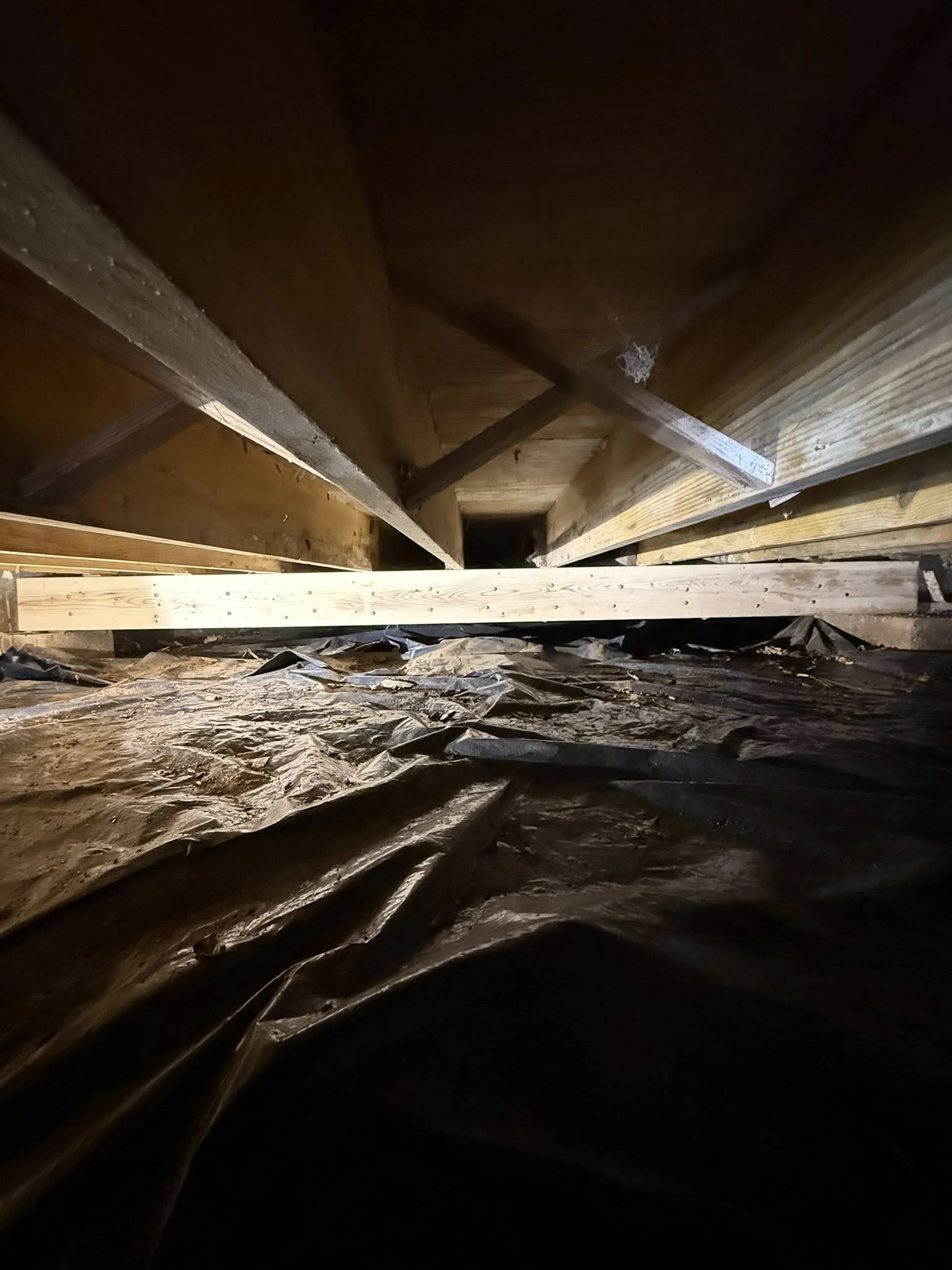Empty attic with exposed wooden beams and black plastic moisture barrier on the floor.