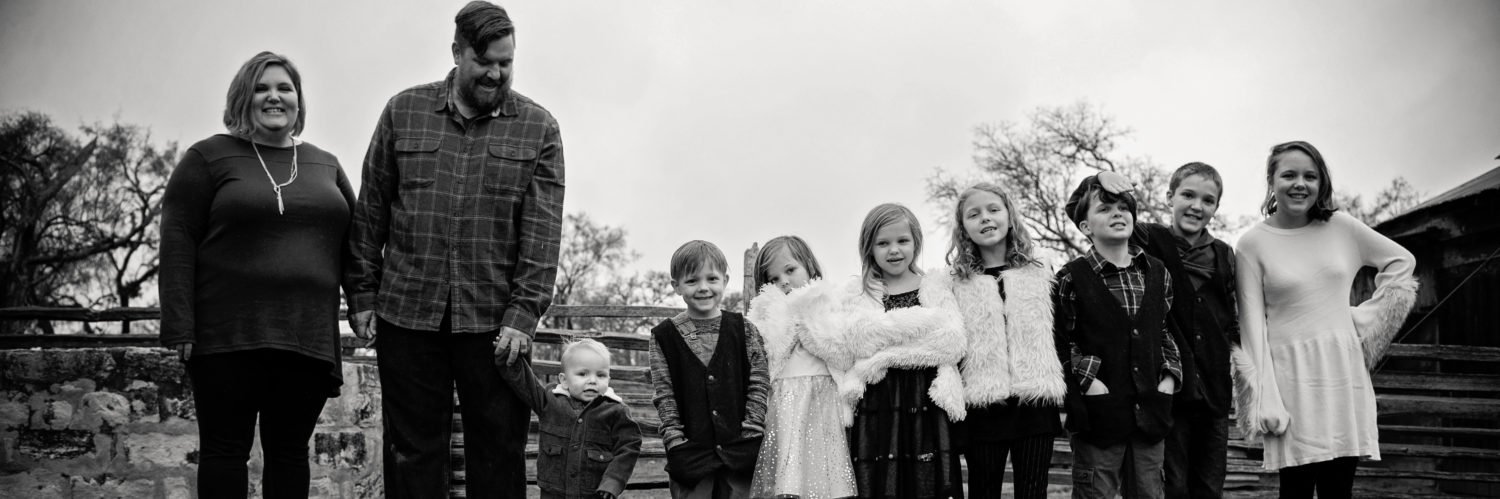 Group of nine people, including adults and children, standing outdoors on steps, smiling and posing for a photo in black and white.
