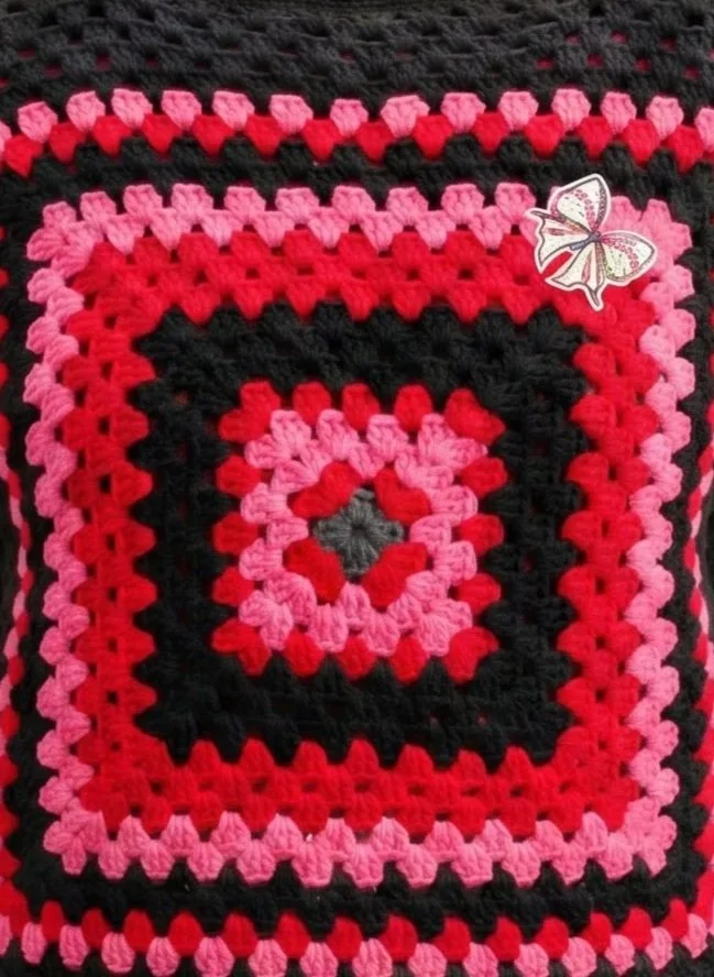  "The Club ColorBlock Sweater"-A statement granny square in bold pink, coral, and black. Finished with a signature bow—texture, rhythm, unmistakable presence.  
 Available by Commission 