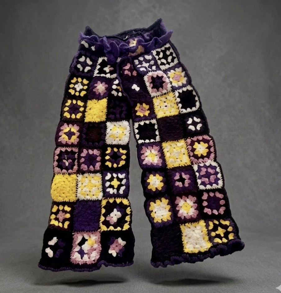 A pair of colorful crocheted scarves with various flower and heart patterns in purple, yellow, pink, white, and black, displayed against a gray background.