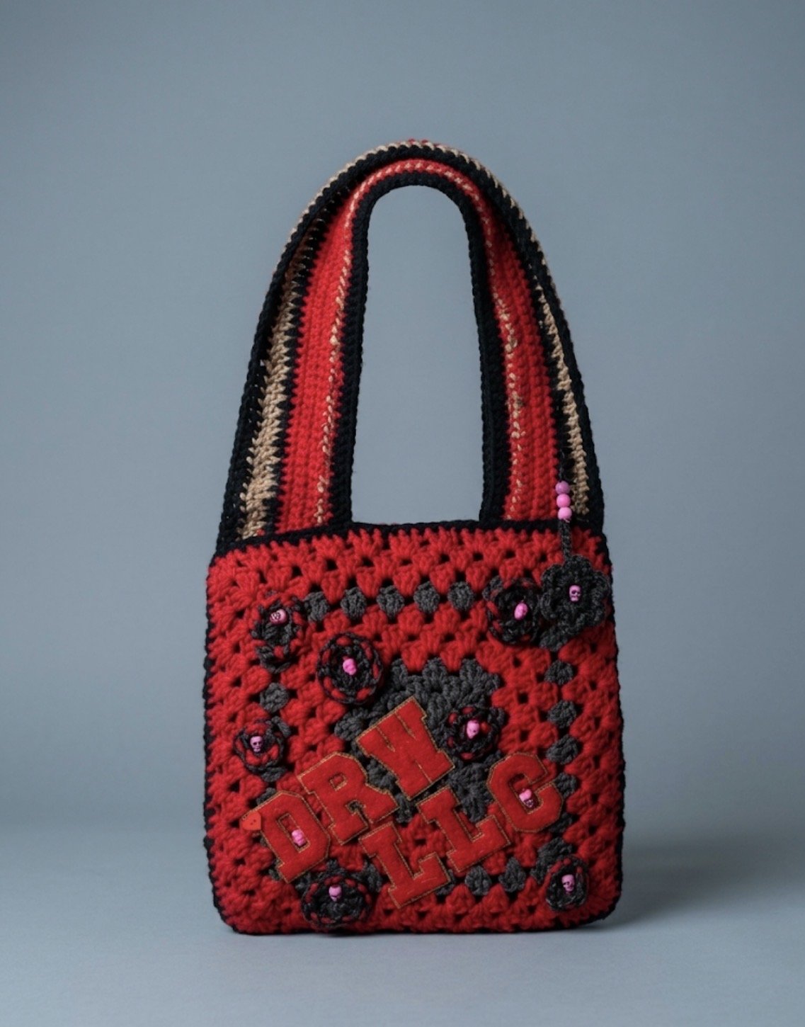 Crocheted handbag in red, black, and beige with the phrase 'DRI LL T' embroidered and decorative flowers with pink beads.