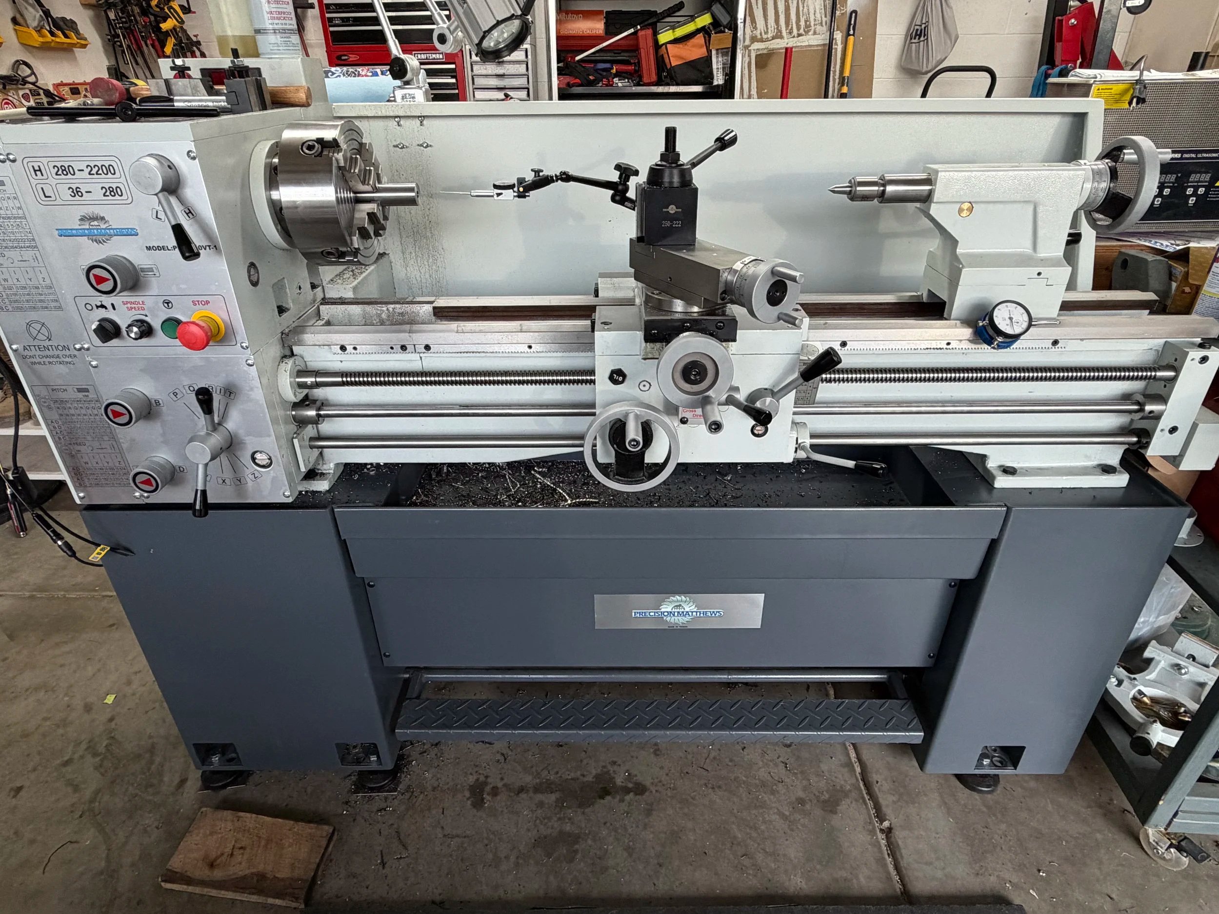 A metal lathe machine in a workshop with various tools and equipment in the background.