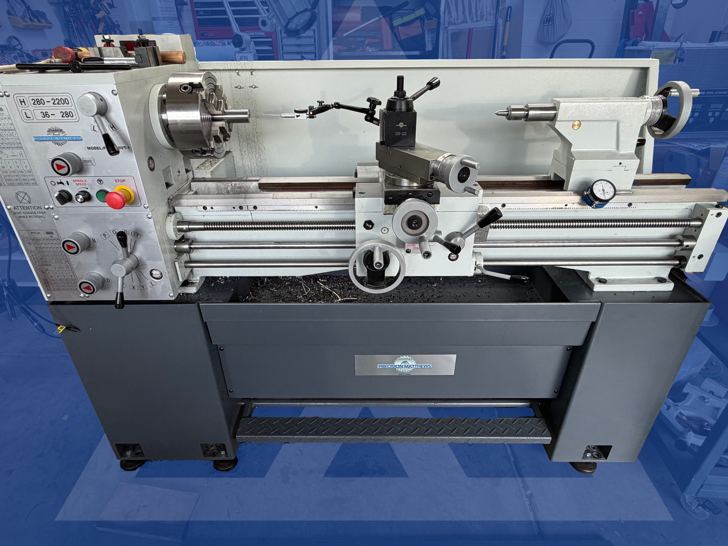 A metal lathe machine in a workshop, with various knobs, dials, and components.