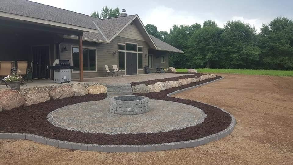 Backyard with stone fire pit, concrete patio, outdoor seating, and a garden bed with dark mulch.