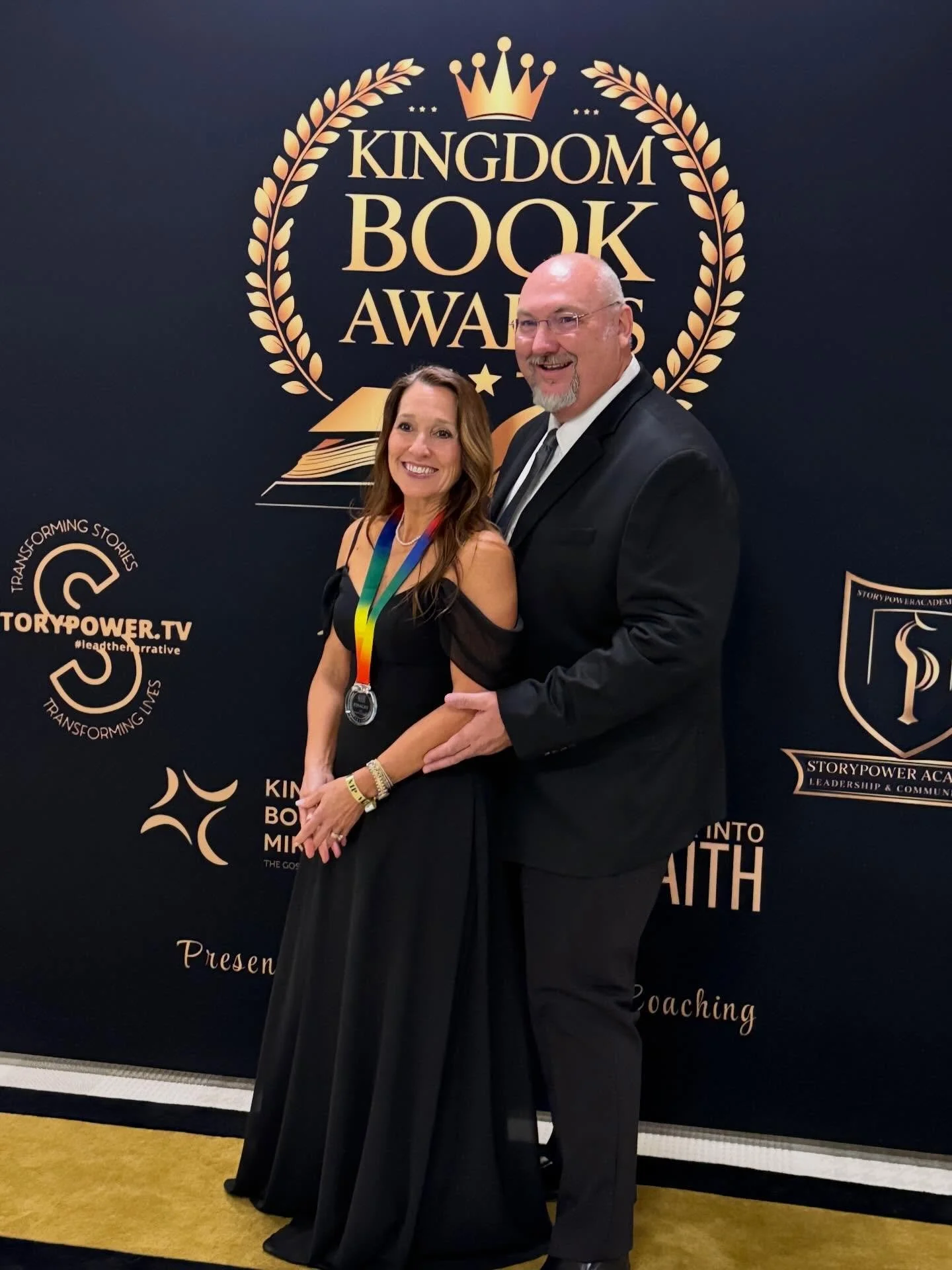 Courtney and Rhonda Smith, standing in front of a black backdrop with gold text and logos related to the Kingdom Book Awards and StoryPower Academy.