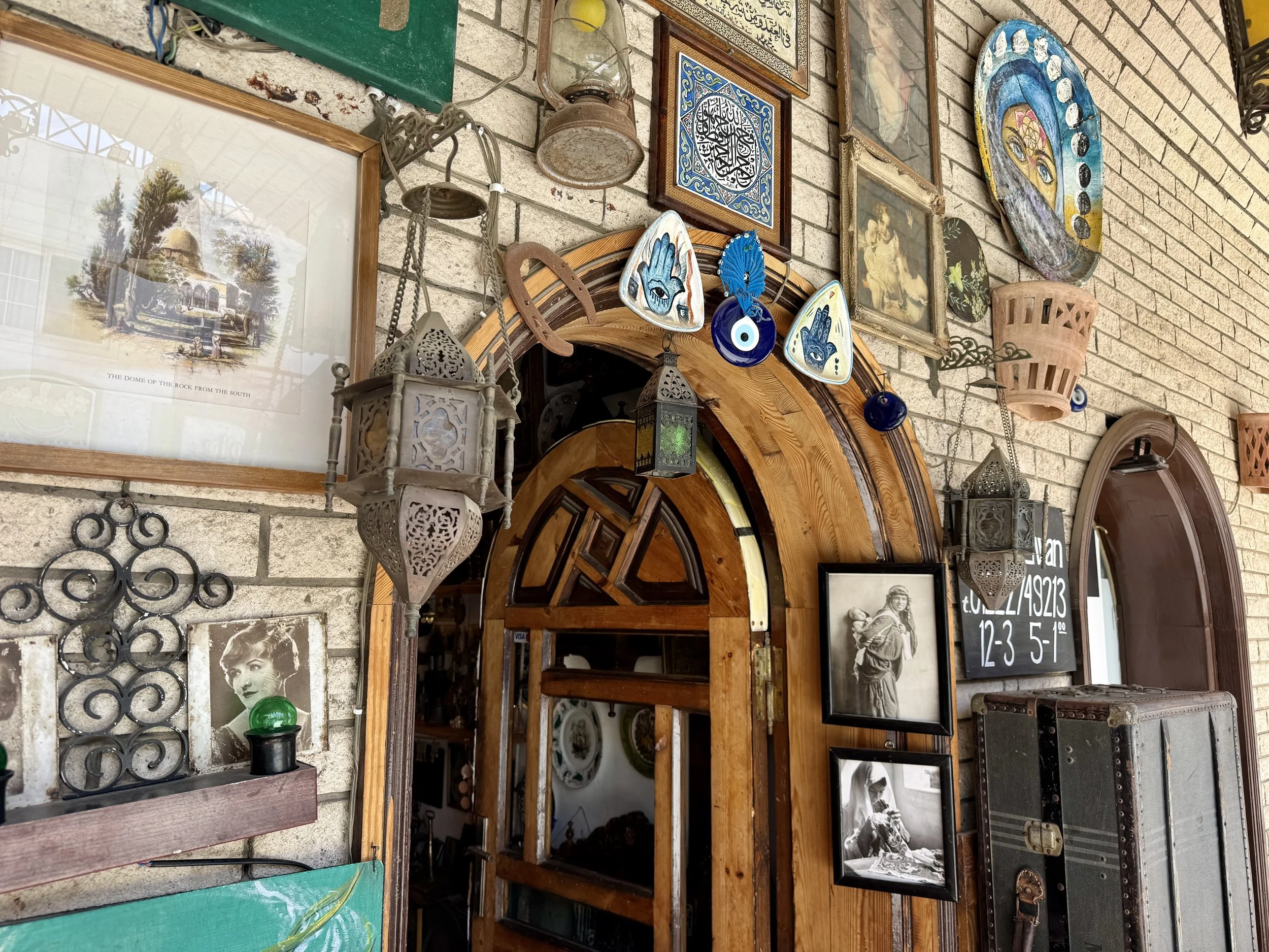 A store or antique shop wall decorated with framed art, paintings, and various decorative items including lanterns, ceramic plates, and photographs.