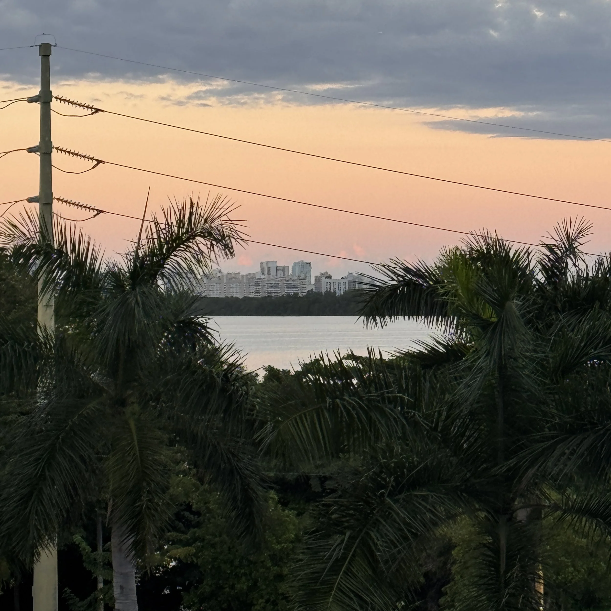 Sunset sky with orange and gray clouds above power pole and palm trees in the foreground.