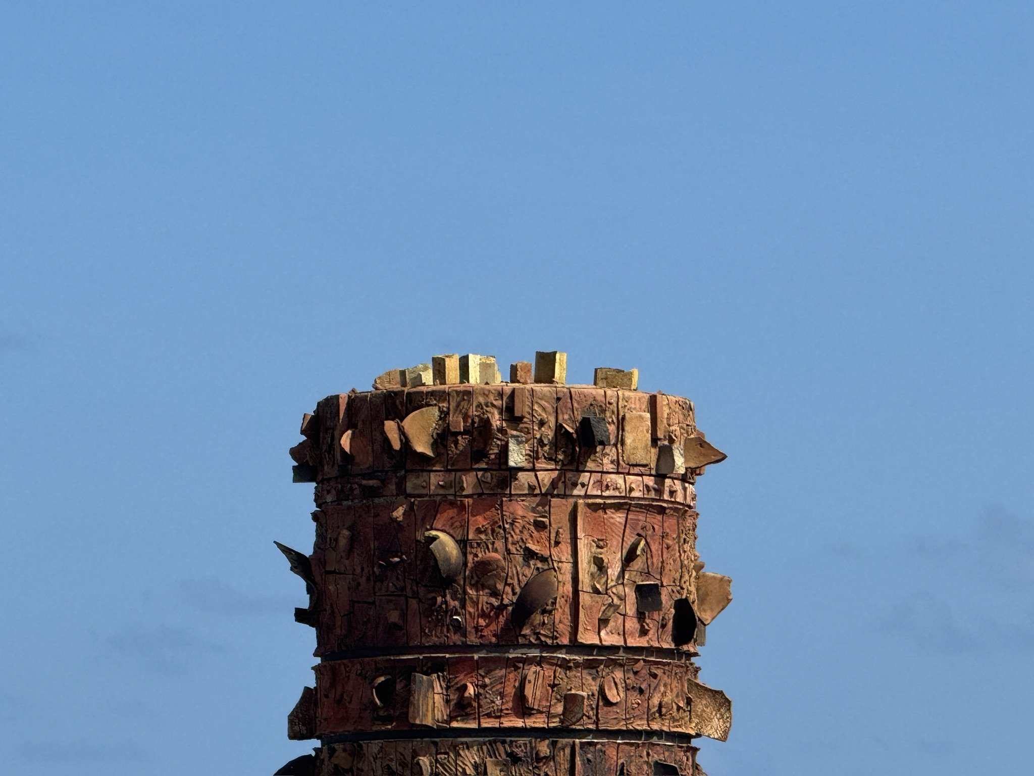 Close-up of a large, weathered brick chimney against a clear blue sky.
