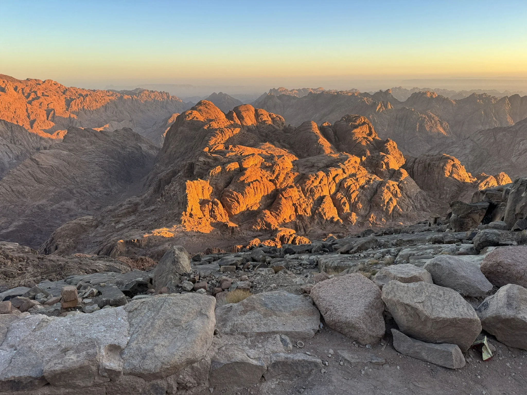 Sunset over a rocky desert landscape with mountains in the background and a clear sky.