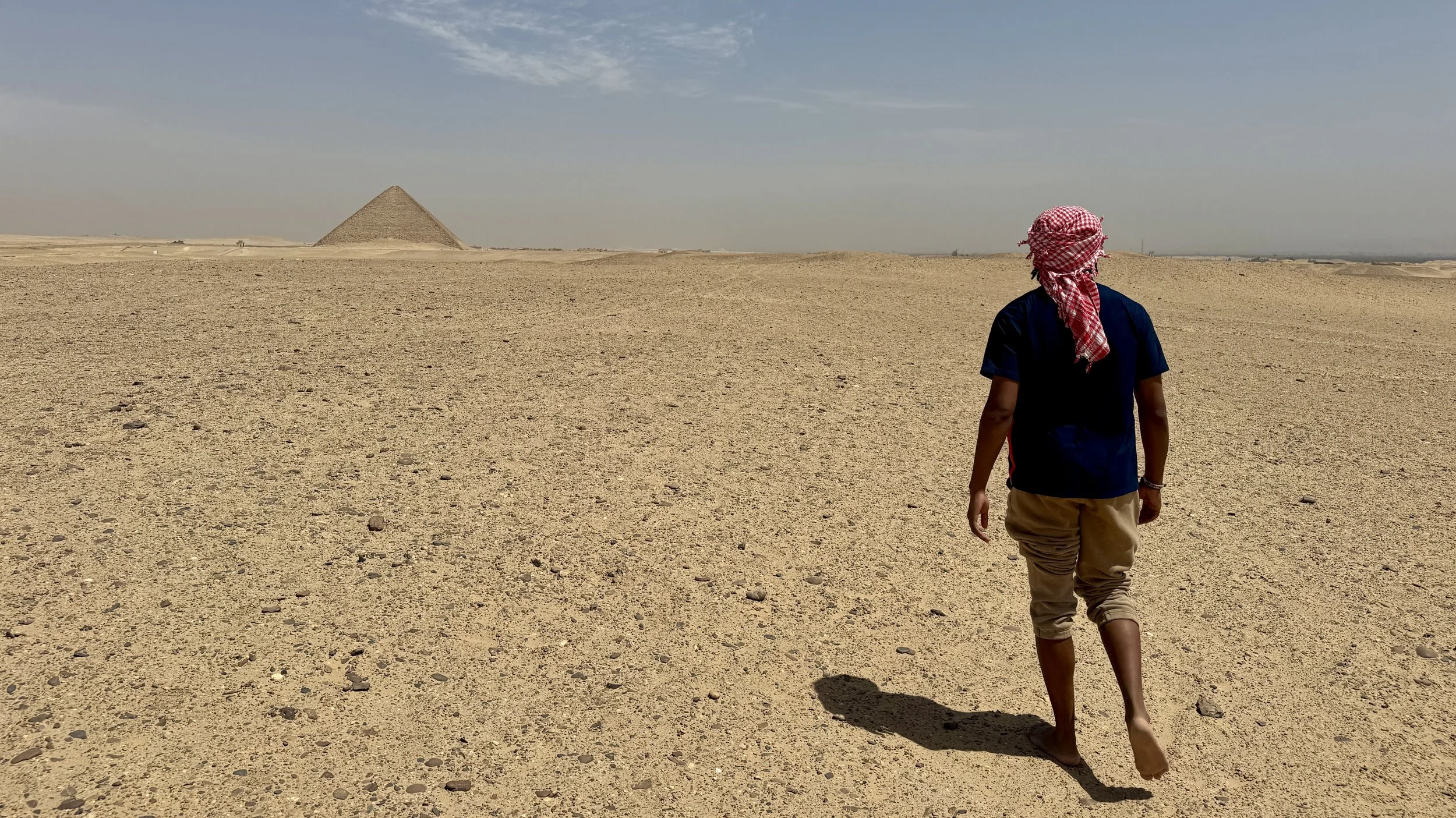 A person walking in a desert landscape with a pyramid in the distance.