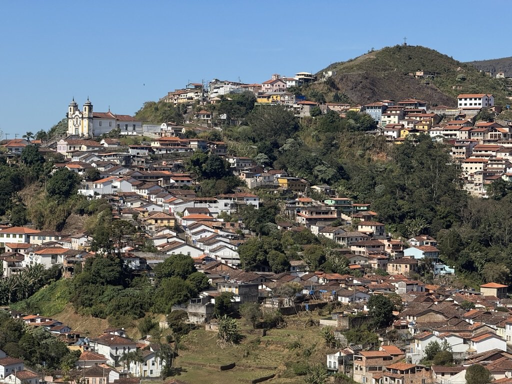 Hilly residential neighborhood with houses, trees, and a church with twin towers in the foreground.