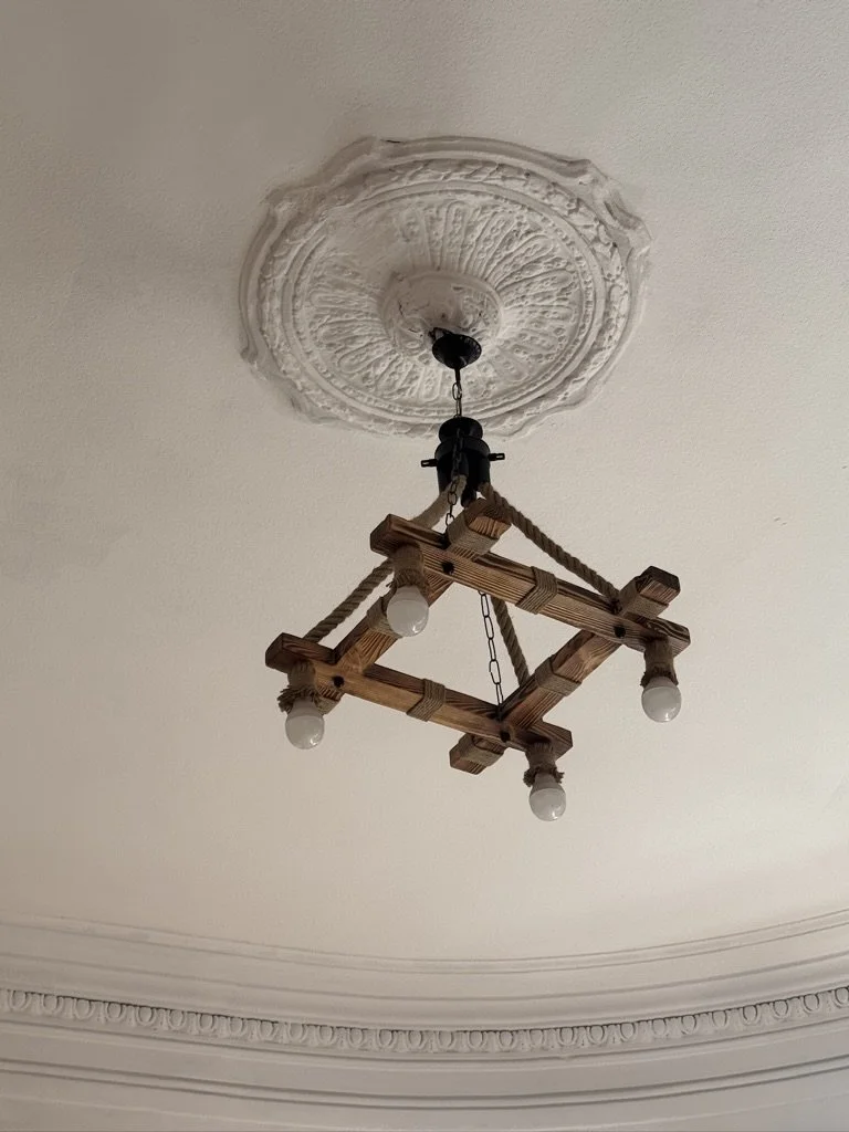 A ceiling with ornate decorative molding and a rustic wooden chandelier with four exposed light bulbs hanging from chains.