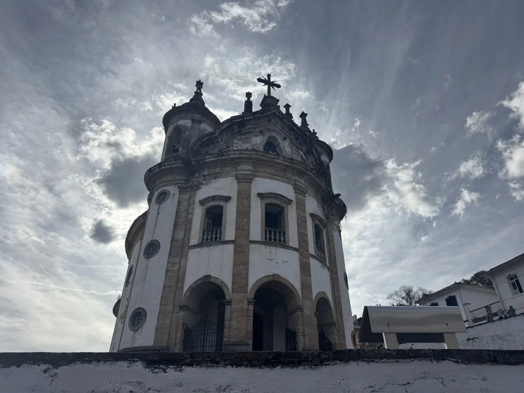 A historic white church with a dome and cross at the top, set against a cloudy sky.