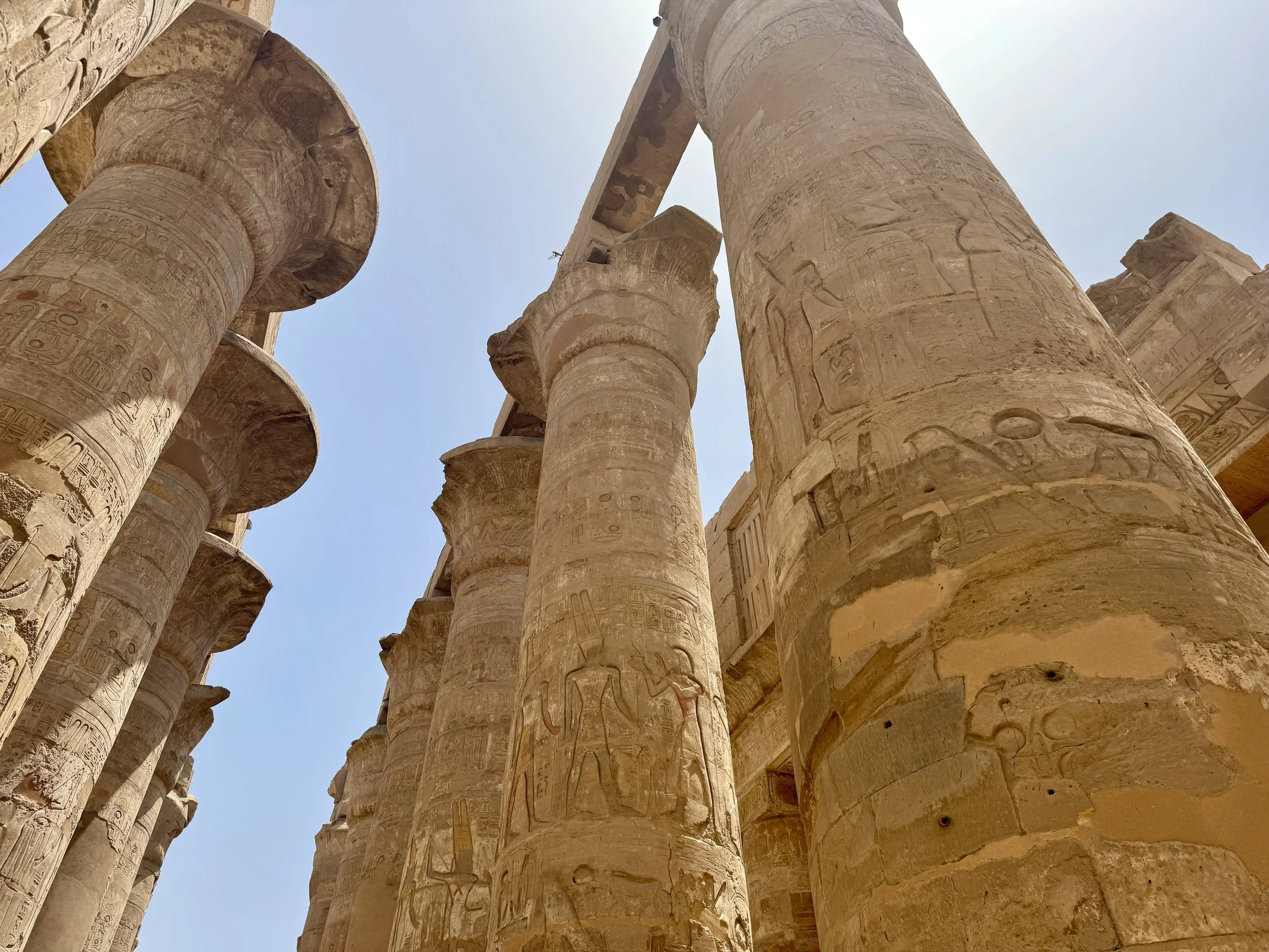 Ancient Egyptian stone columns with hieroglyphic carvings, under a clear blue sky.
