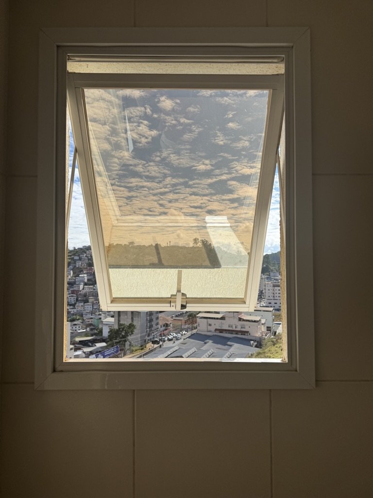 Open skylight window with view of a cloudy sky and cityscape below.
