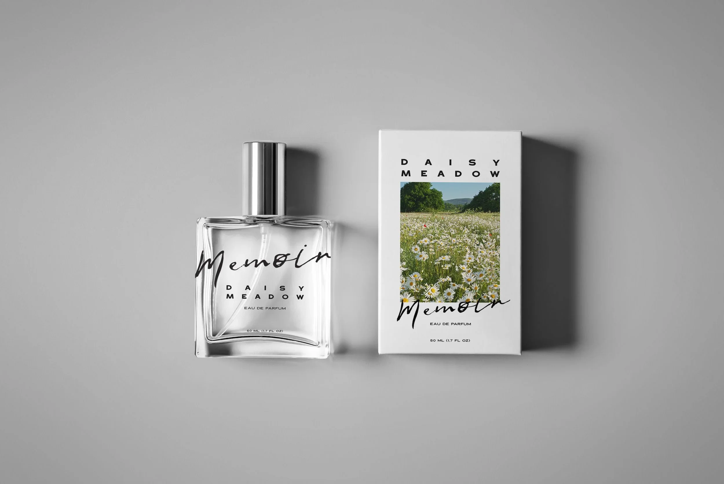 A perfume bottle labeled 'Memori' and its packaging box with a scenic meadow image, both on a gray background.