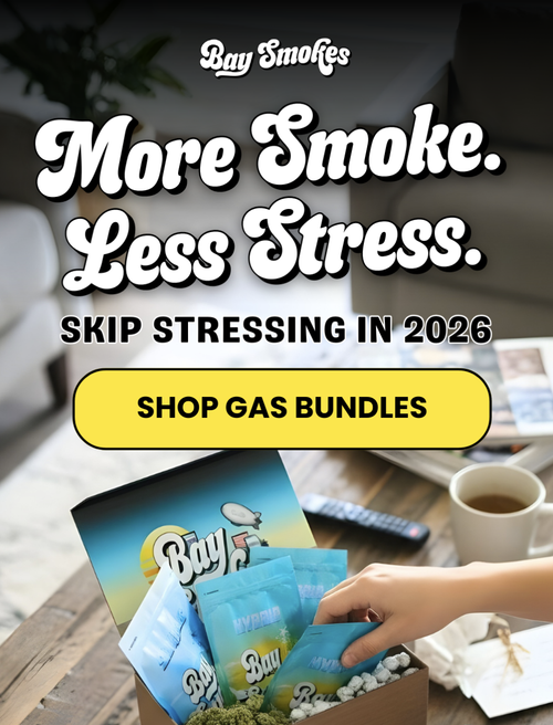 Advertisement for Bay Smokes featuring the message 'More Smoke. Less Stress.' with a call to action 'Shop Gas Bundles', displaying a hand reaching for cannabis products in a blue box on a wooden table, with a coffee mug and remote in the background.
