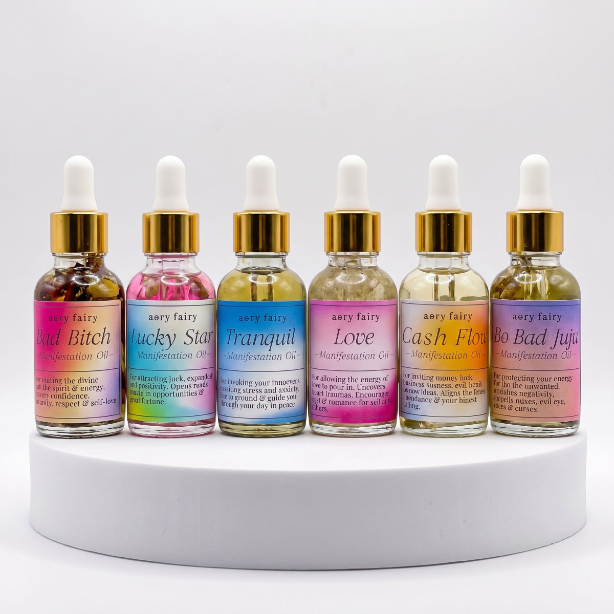 Six small glass bottles with dropper caps, labeled with different colors and names, containing manifestation oils.