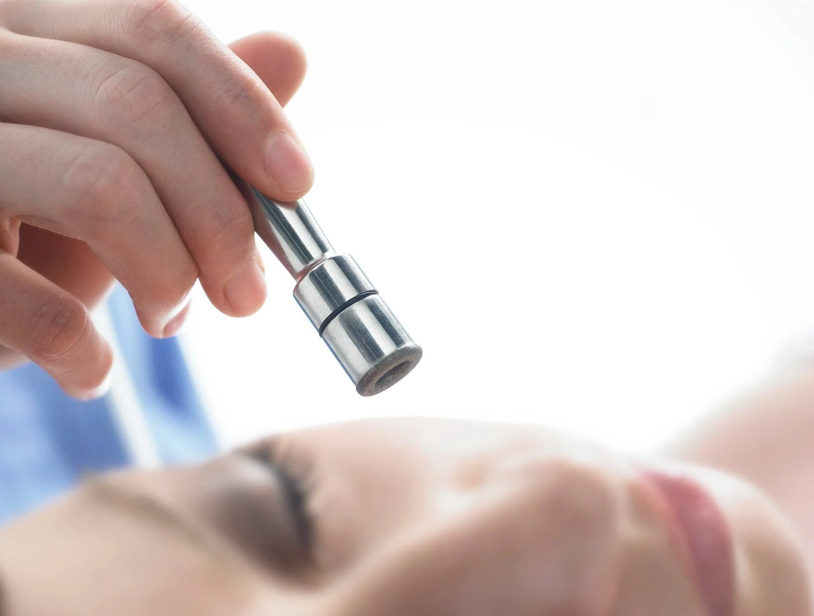 Close-up of a hand holding a metal wand over a clients skin for diamond microdermabrasion.
