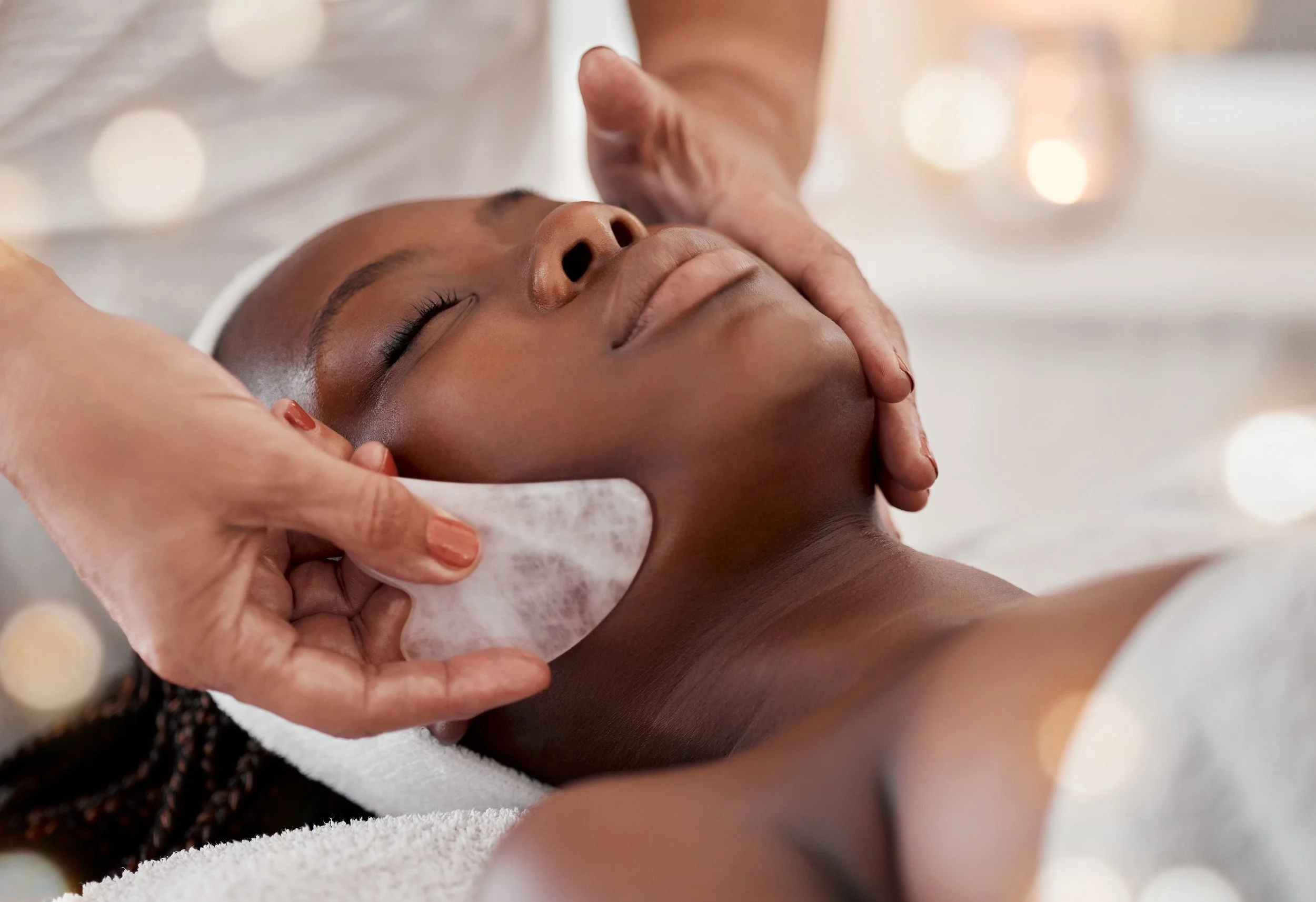A person receiving a gua sha massage in a clinical setting, with closed eyes and a relaxed expression.