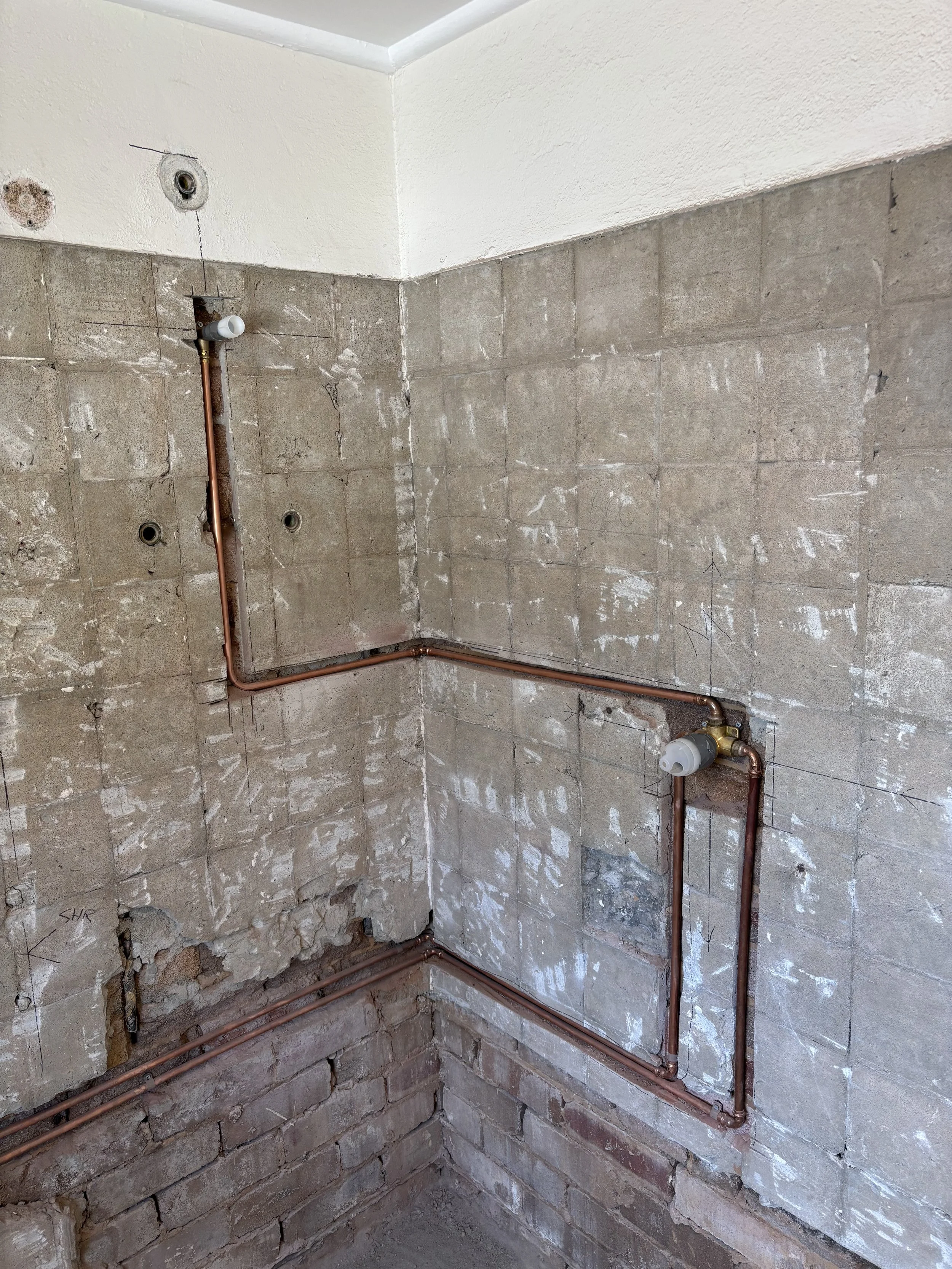Construction or renovation site showing exposed brick walls, plumbing pipes, and unfinished surfaces.