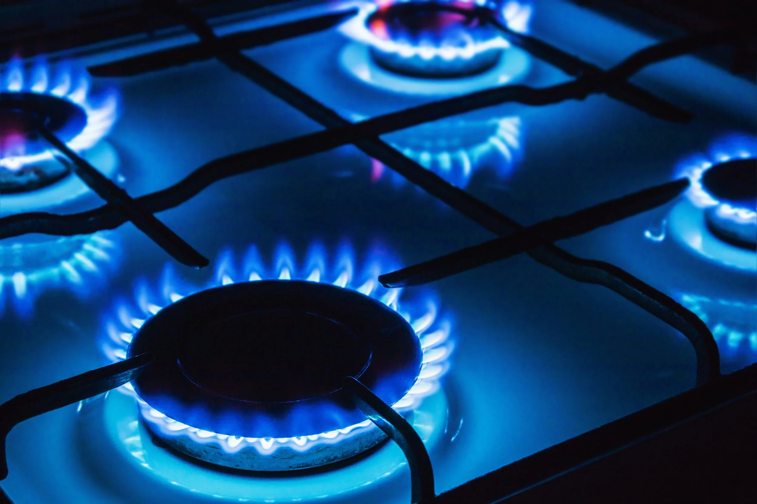 Close-up of a lit gas stovetop burner with blue flames and black grates.