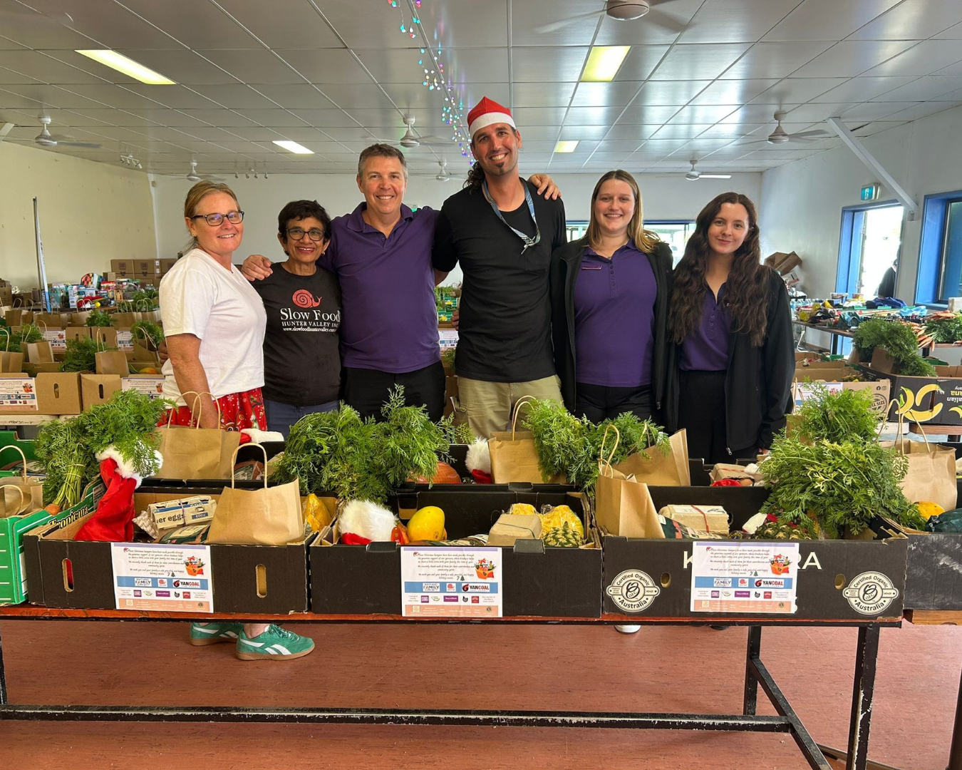 Six people standing behind a table with vegetable boxes, for a community support program with Richard Stark