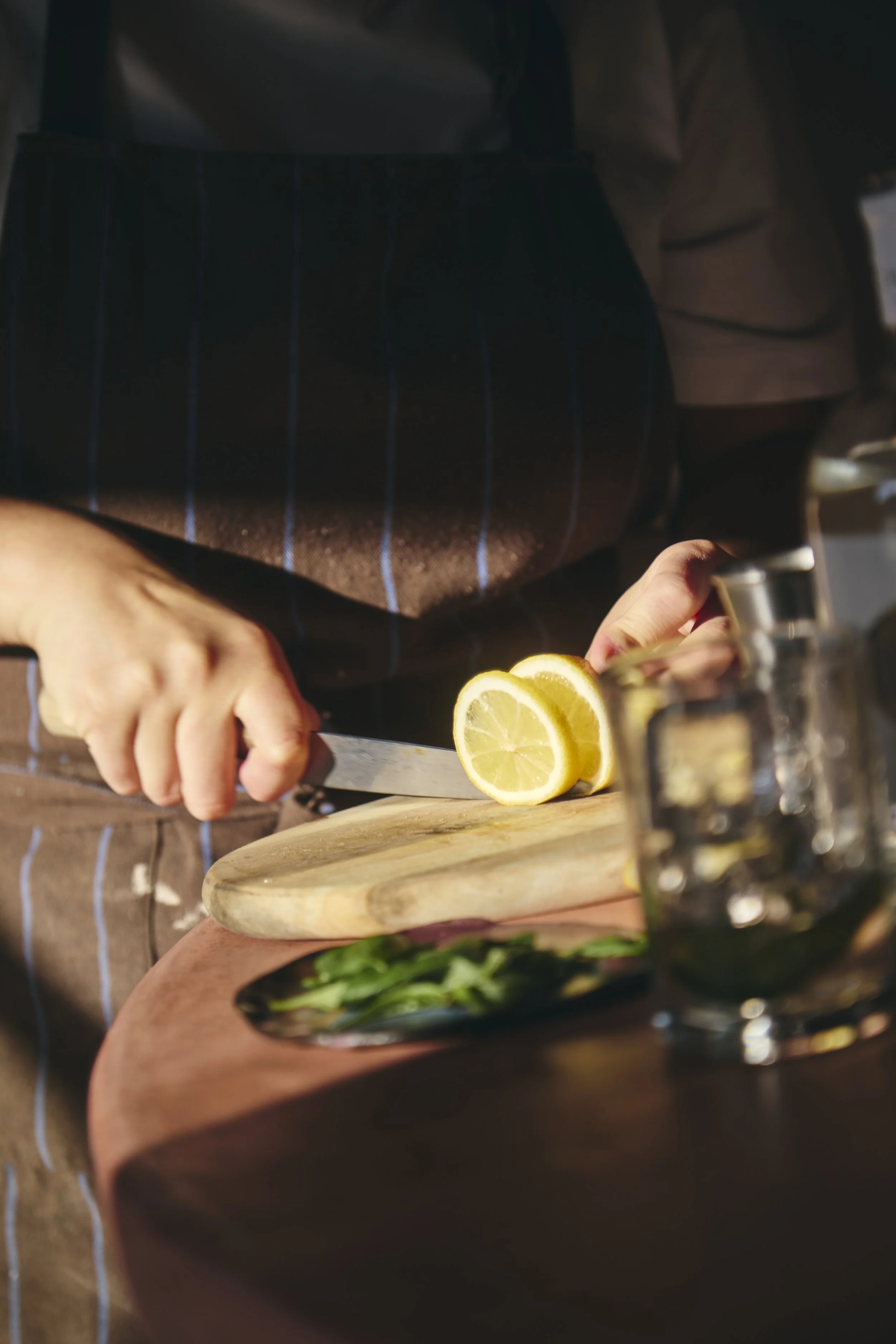 Person slicing lemon on a wooden cutting board with a knife.