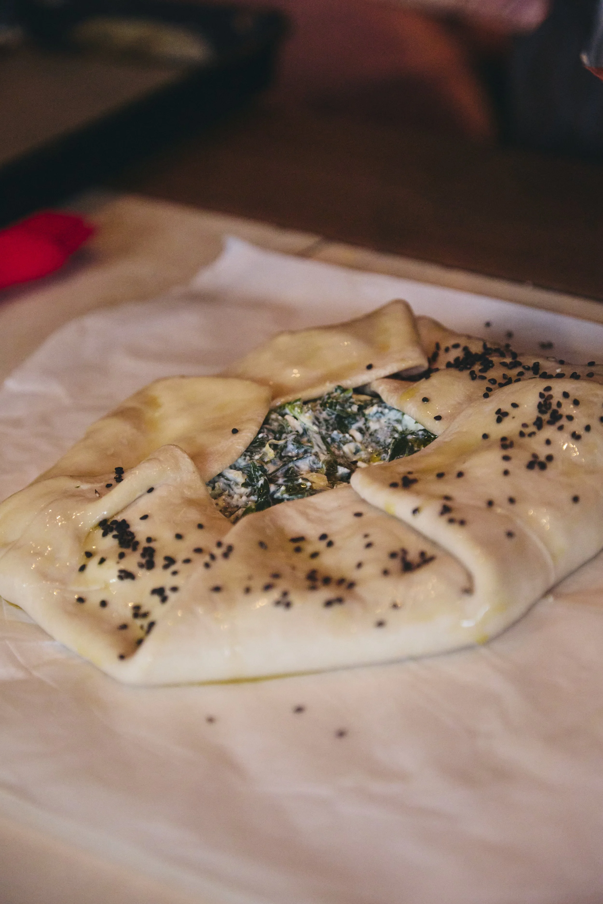 A white rectangular plate with a cooked dish featuring a pastry shell, filled with a spinach and cheese mixture, garnished with black sesame seeds.