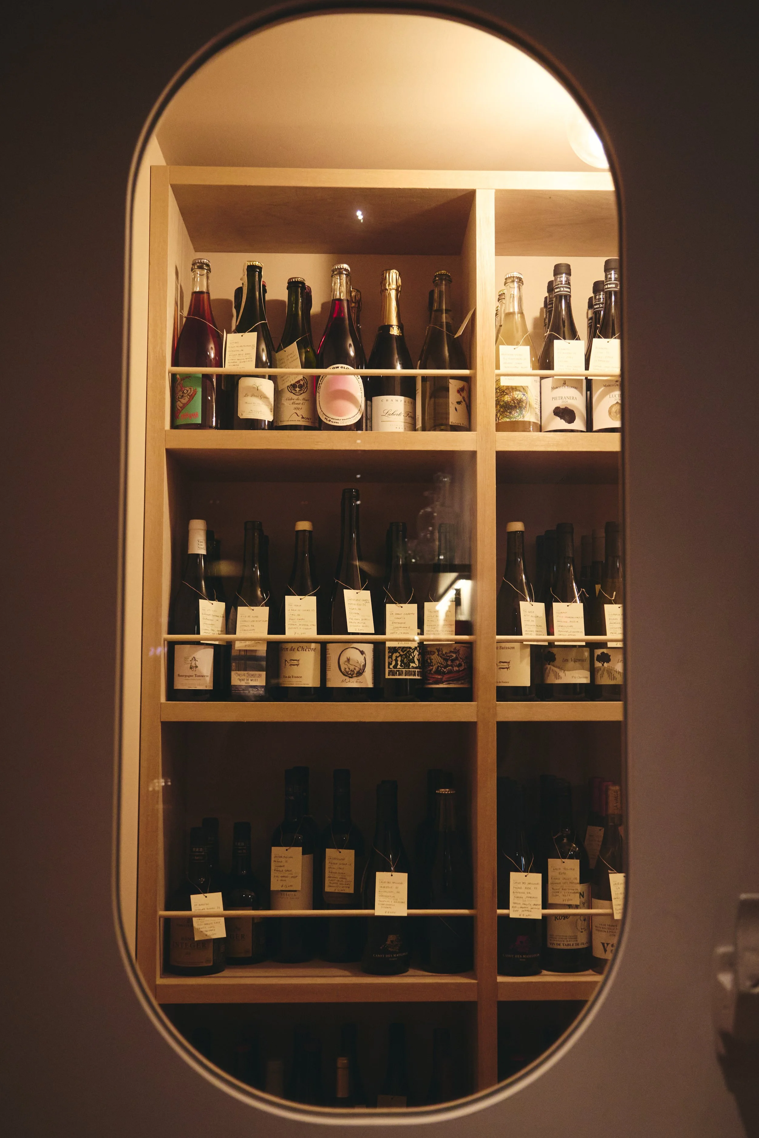 A wooden wine shelf filled with various bottles of wine, seen through a circular opening.
