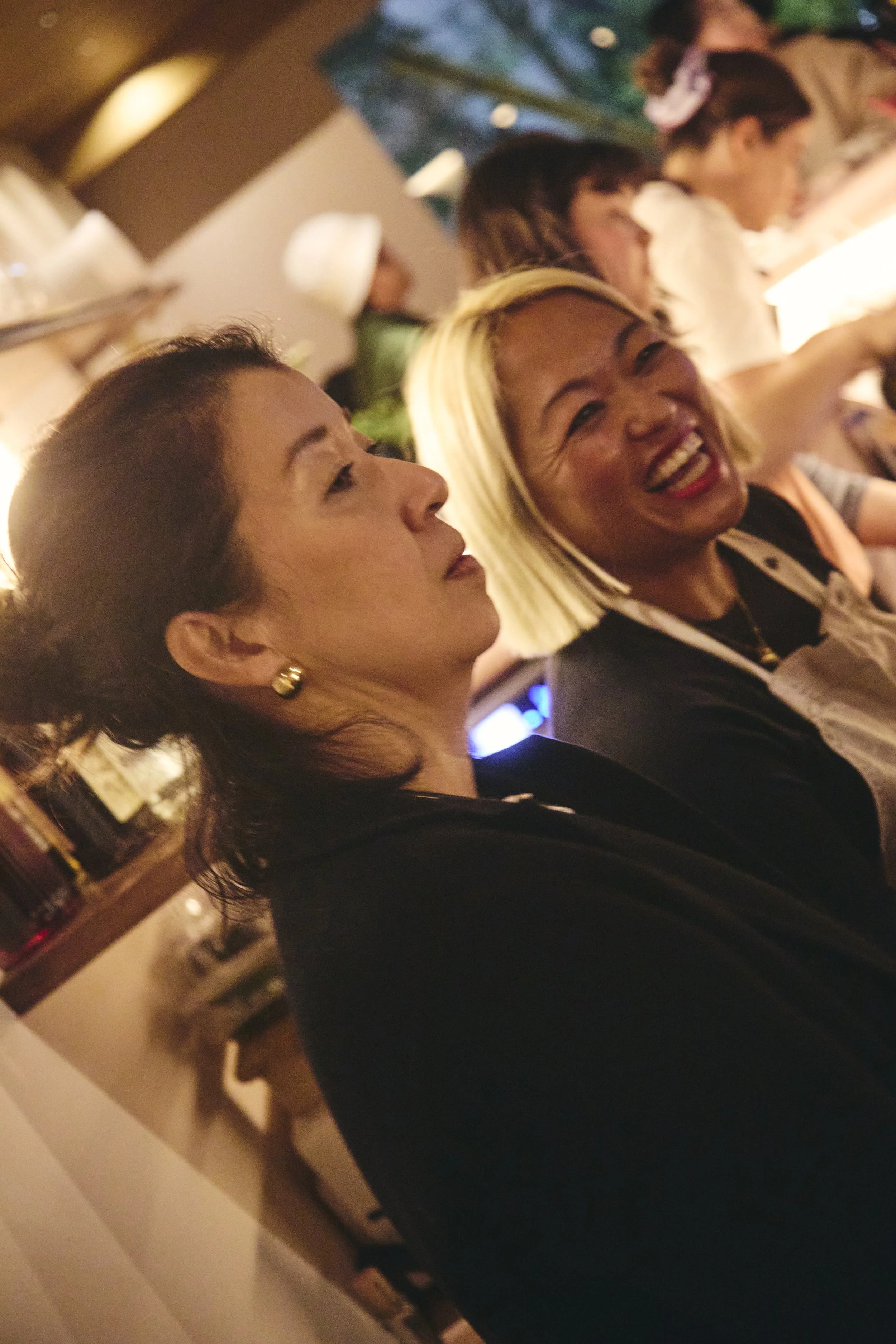 Several women are sitting at a dining table in a dimly lit restaurant, smiling and talking to each other.