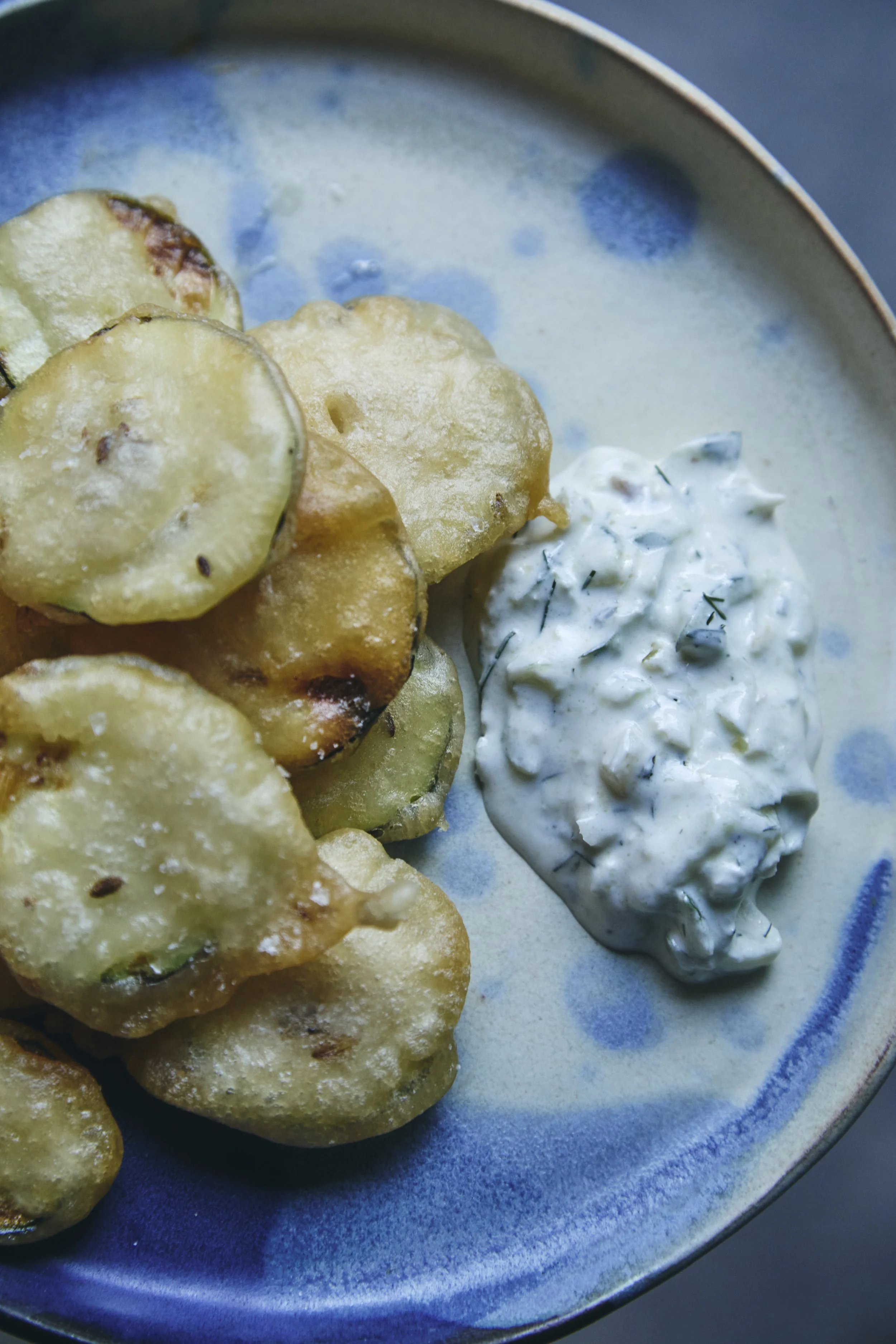 Fried green tomatoes served on a blue ceramic plate with a side of creamy herb sauce garnished with dill.