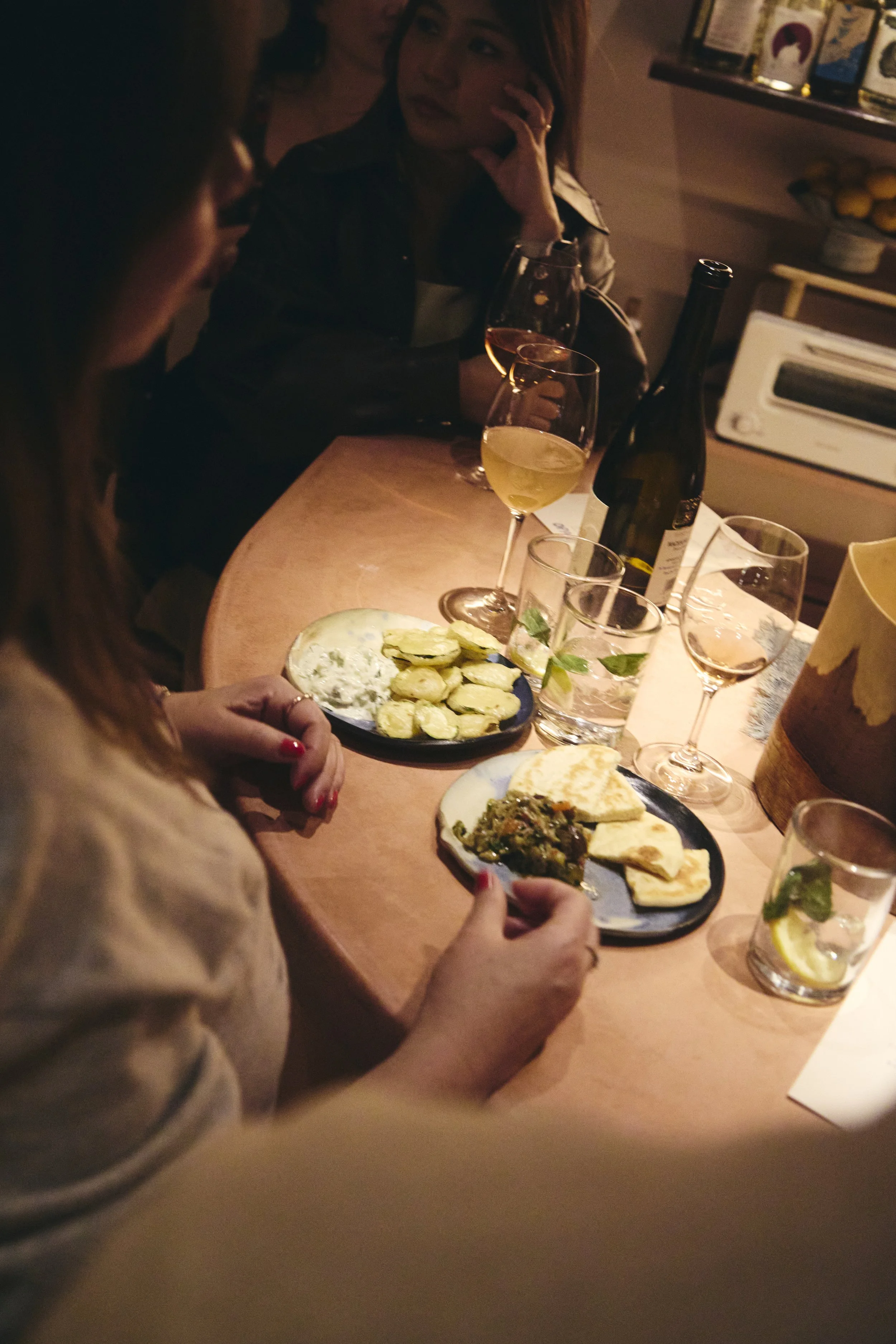People gathered around a table enjoying drinks and food in a dimly lit setting, possibly a restaurant or bar.