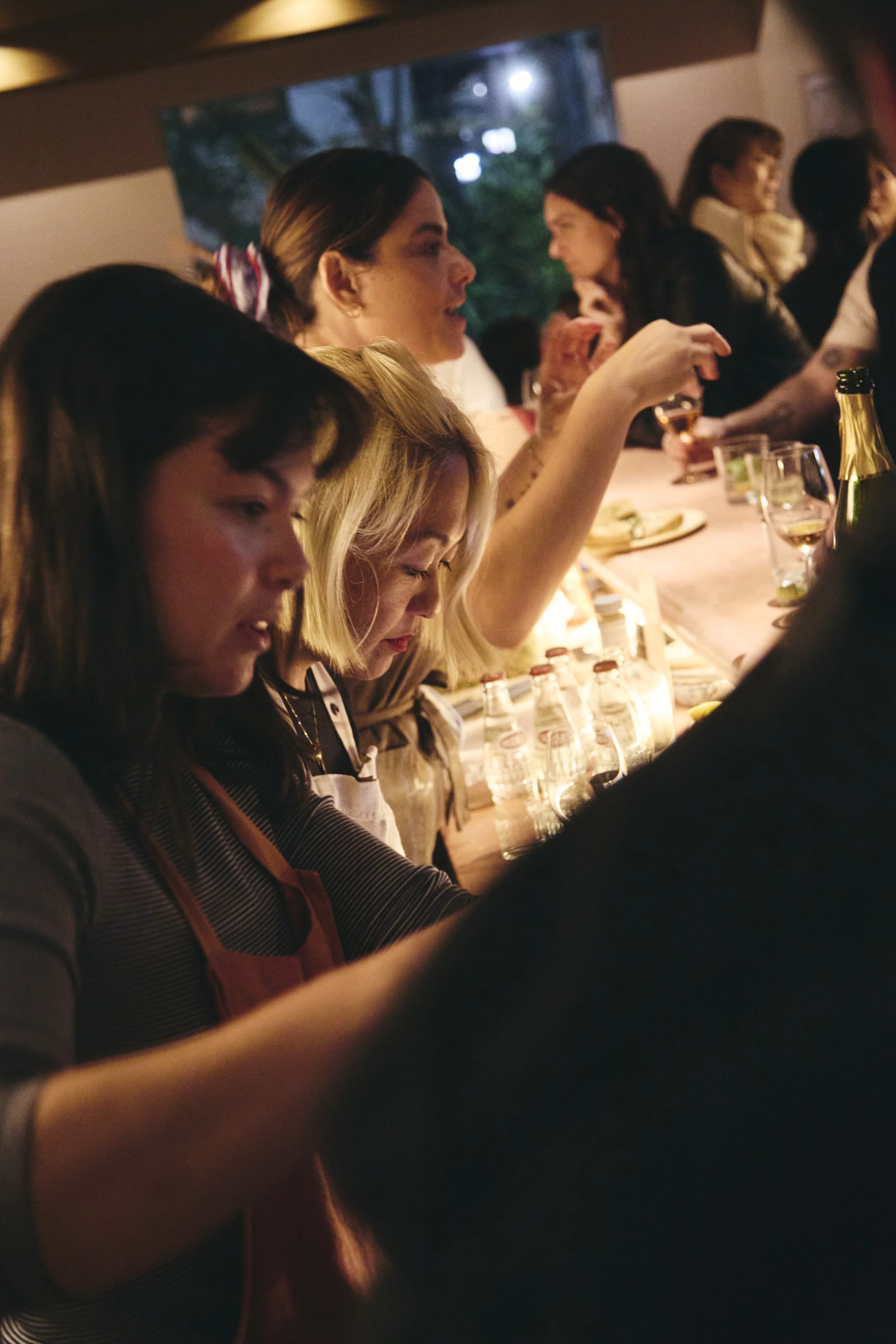 People gathered around a bar or counter, engaging in conversation and enjoying food and drinks in a cozy indoor setting.