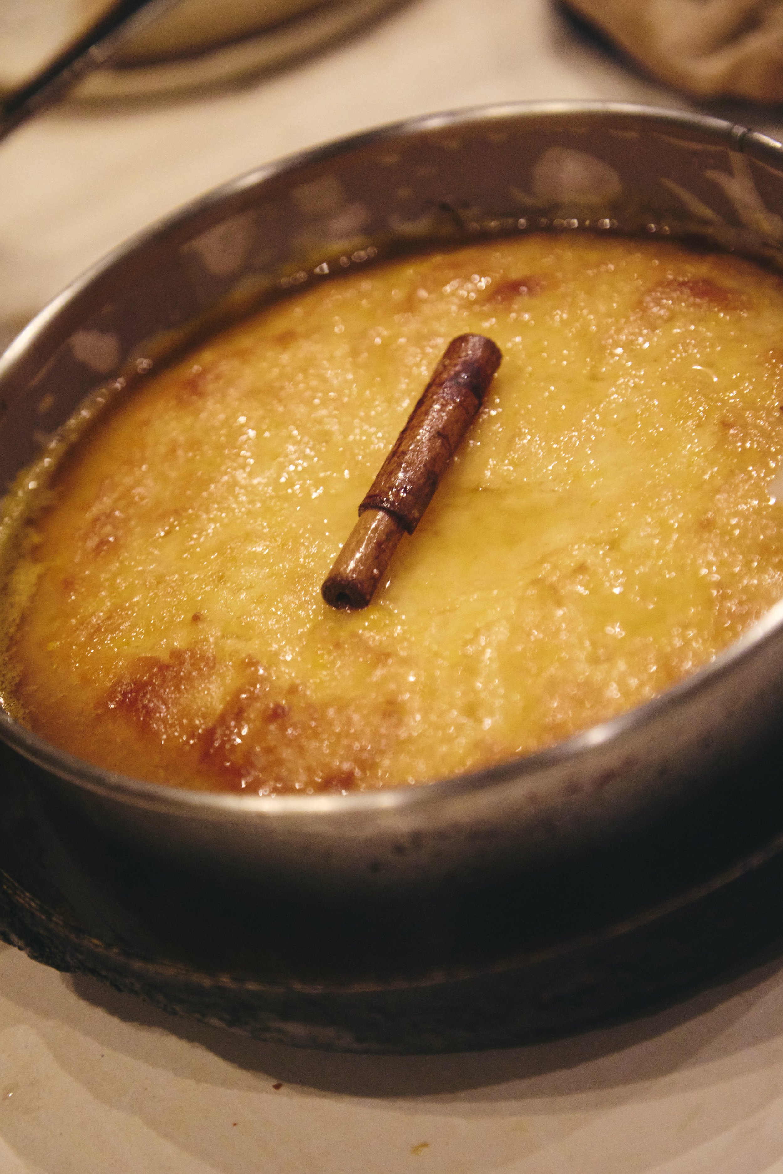 A close-up of a baking dish with a baked dessert topped with a cinnamon stick.