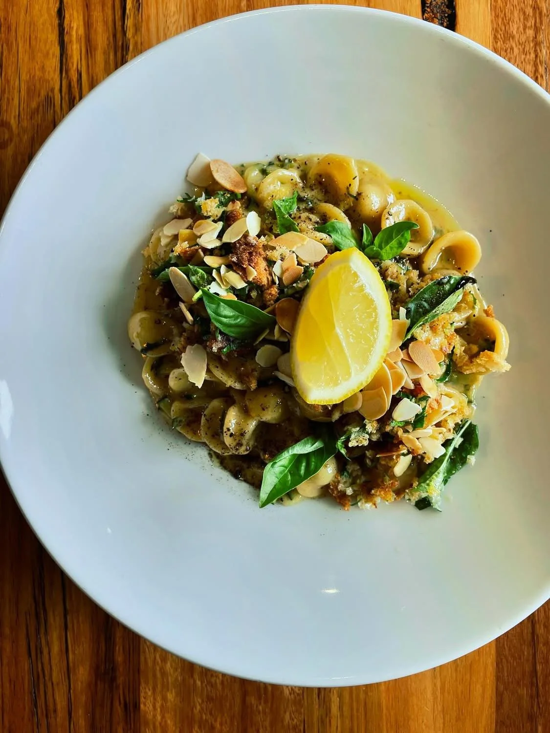 A plate of pasta garnished with lemon wedge, basil leaves, and sliced almonds.