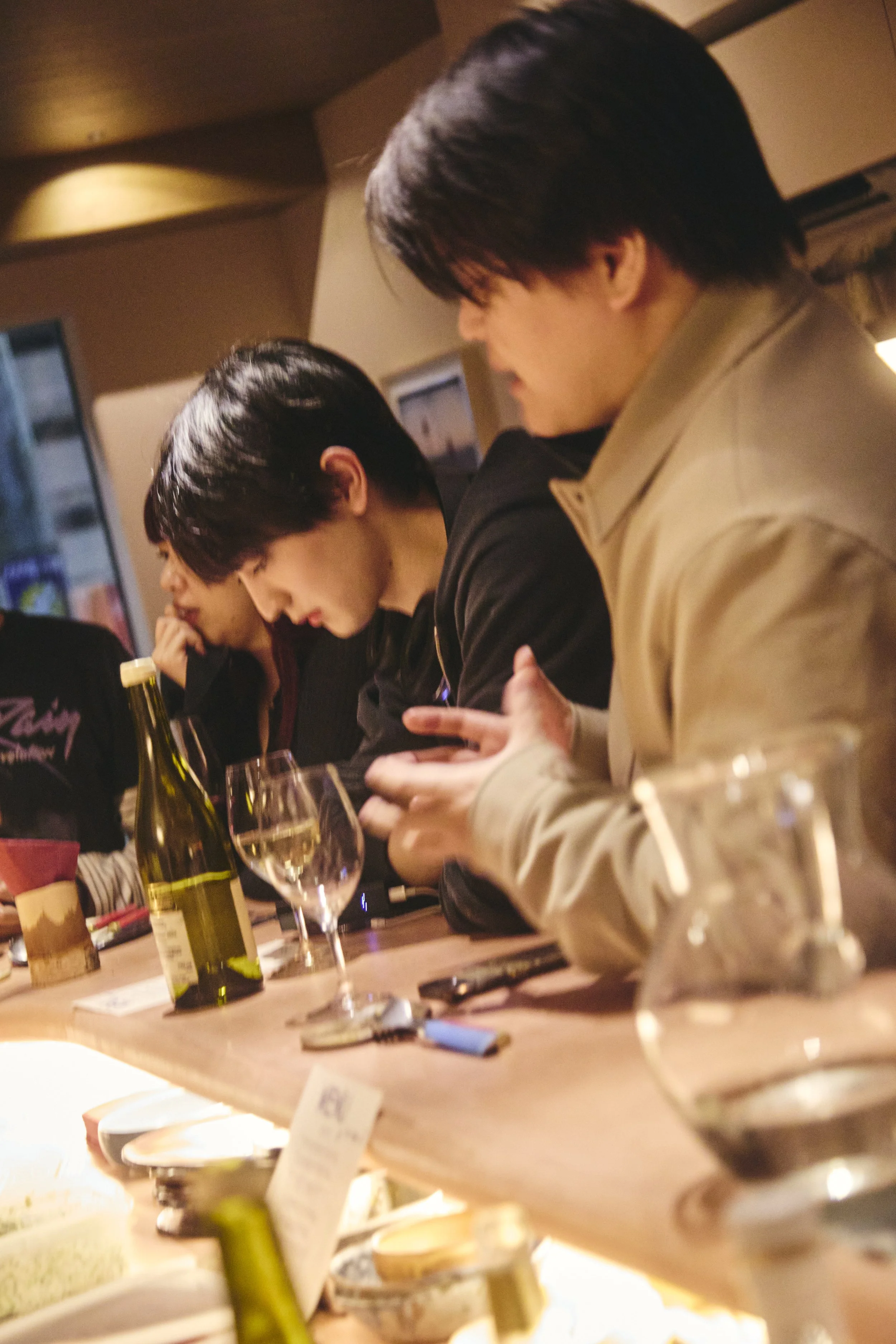 People sitting at a dining table in a restaurant, with drinks and wine bottles visible, engaged in conversation.