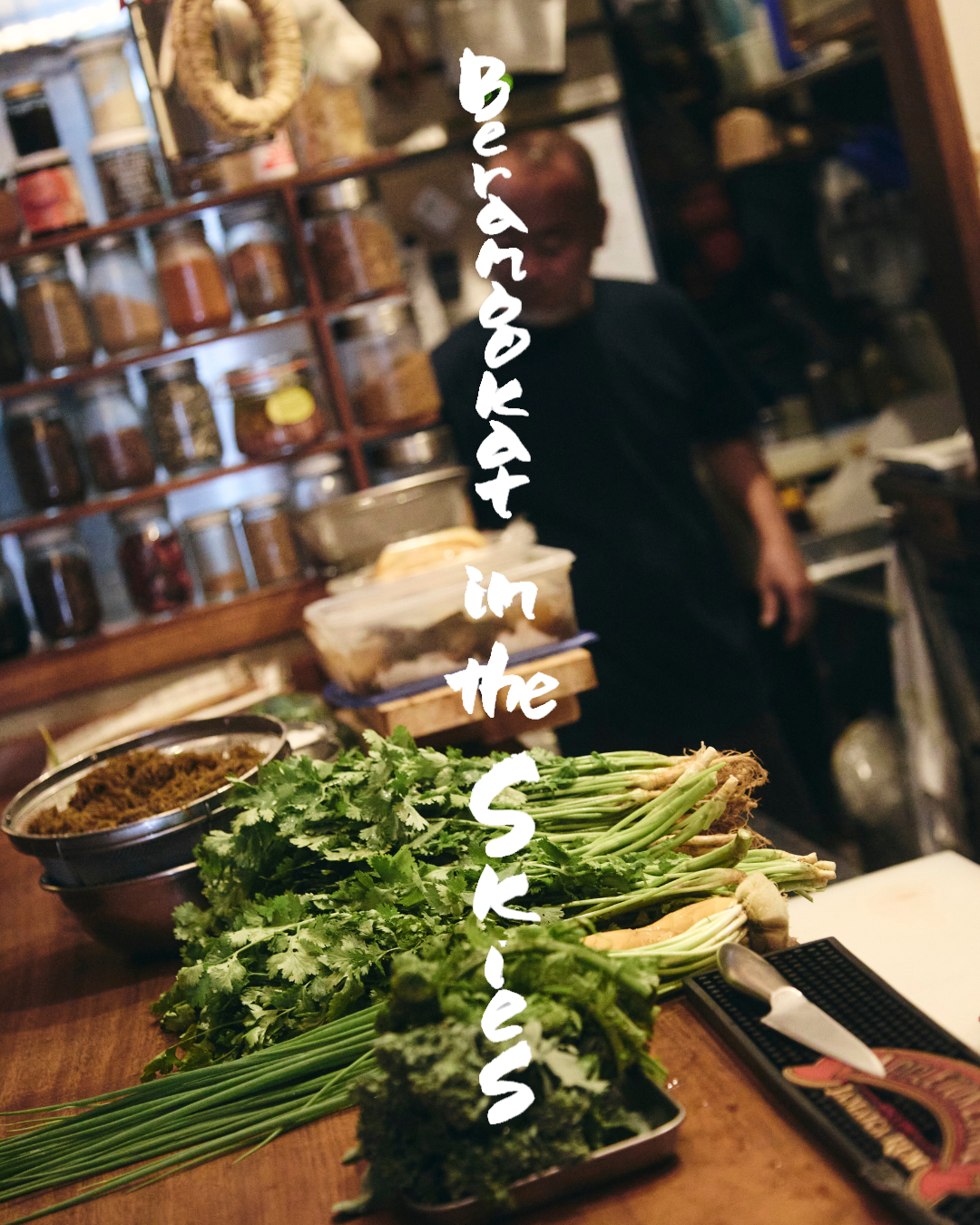 Fresh herbs and vegetables on a kitchen counter with a person in the background, shelves with jars, and the words 'adventures in the sink' written vertically in the center.